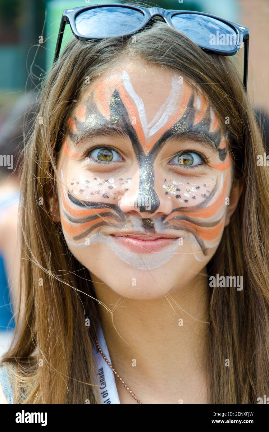 Salsa auf dem St. Saint Clair Festival Szenen: Eine freche junge Frau in katzenähnlicher Gesichtsfarbe grinst an der Kamera. Die schelmisch aussehende Brünette mit braunen Augen Stockfoto