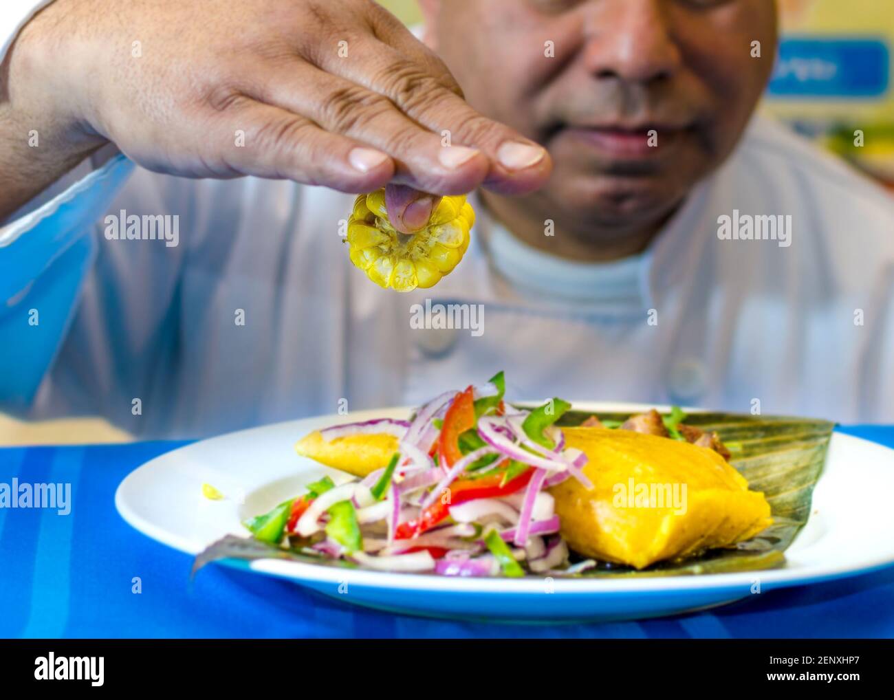 Kubanische Küche: tamal oder Tamales. Der Küchenchef stellt die traditionelle kubanische Mahlzeit auf einem Teller mit blauer Tischdecke dar Stockfoto