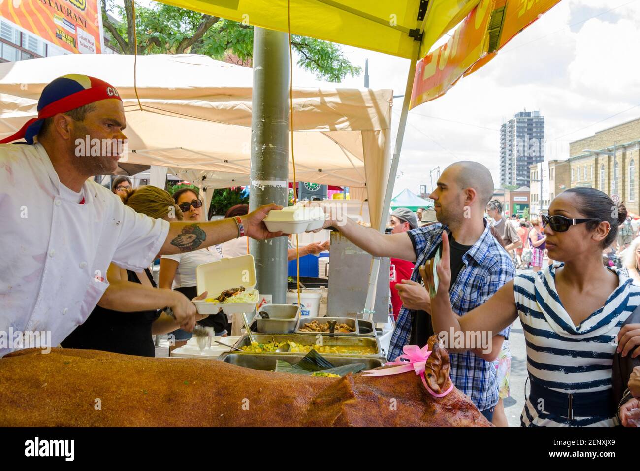 Salsa auf St. Saint Clair Festival Szenen: Ein Koch in einem Kopf-Tuch übergibt einen Behälter mit Lebensmitteln an einen Mann mit einem rasierten Kopf zur gleichen Zeit, dass h Stockfoto