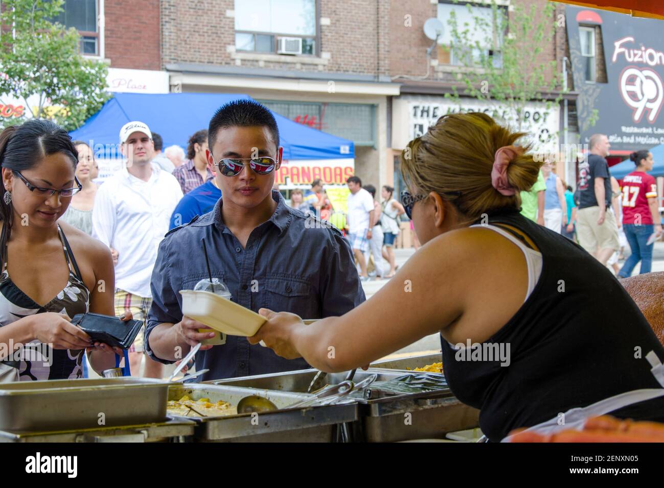 Salsa auf dem St. Saint Clair Festival Szenen: Eine weibliche Serverin zeigt zwei Kunden den Inhalt eines Containers, während eine Dame in einem Haltertop auf ihre wa schaut Stockfoto
