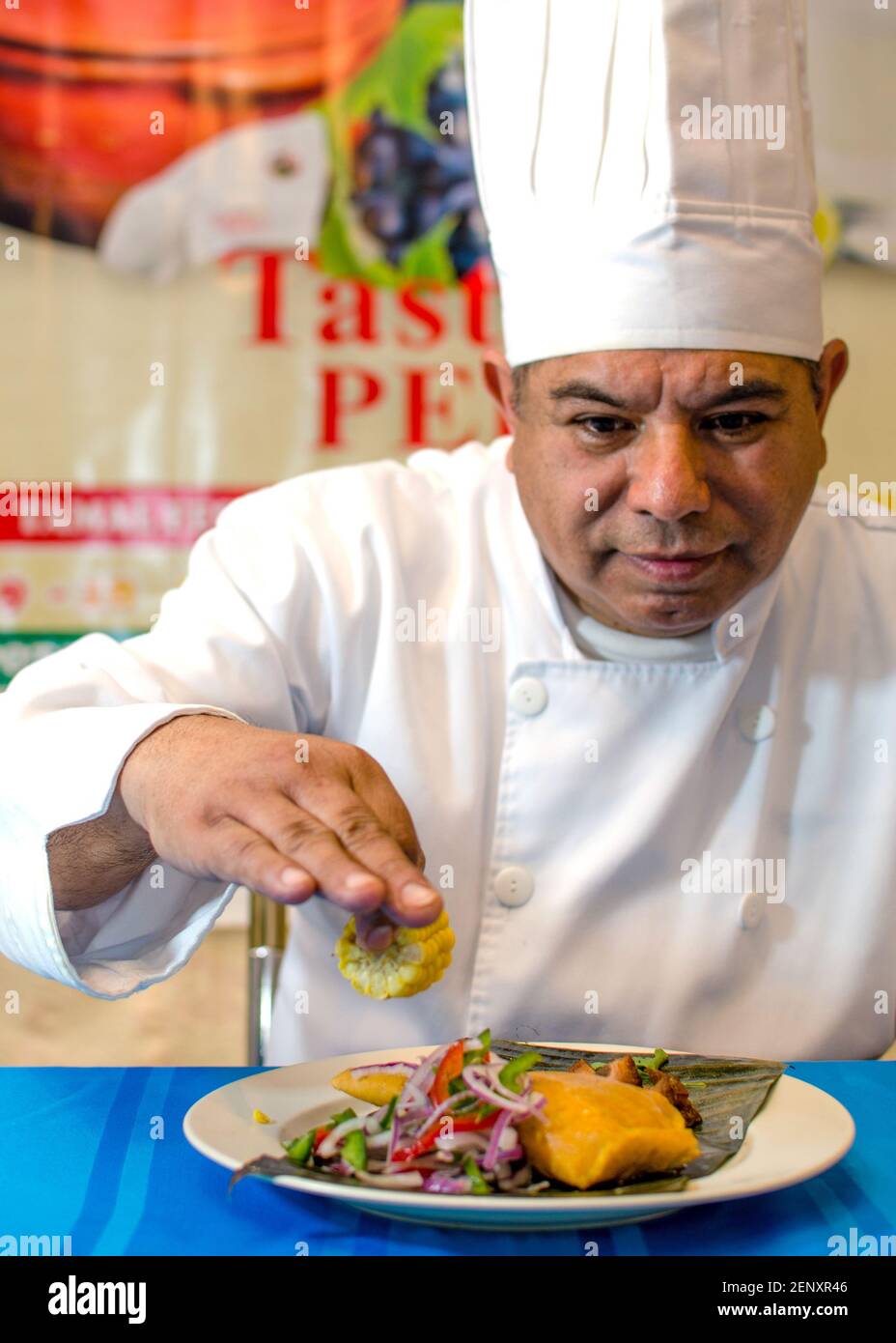 Koch Finishing Teller Tamal. Er trägt ganz weiß und legt den letzten Schliff, eine Zitrone, auf einen Teller Tamal mit einer Seite Gemüse. Stockfoto
