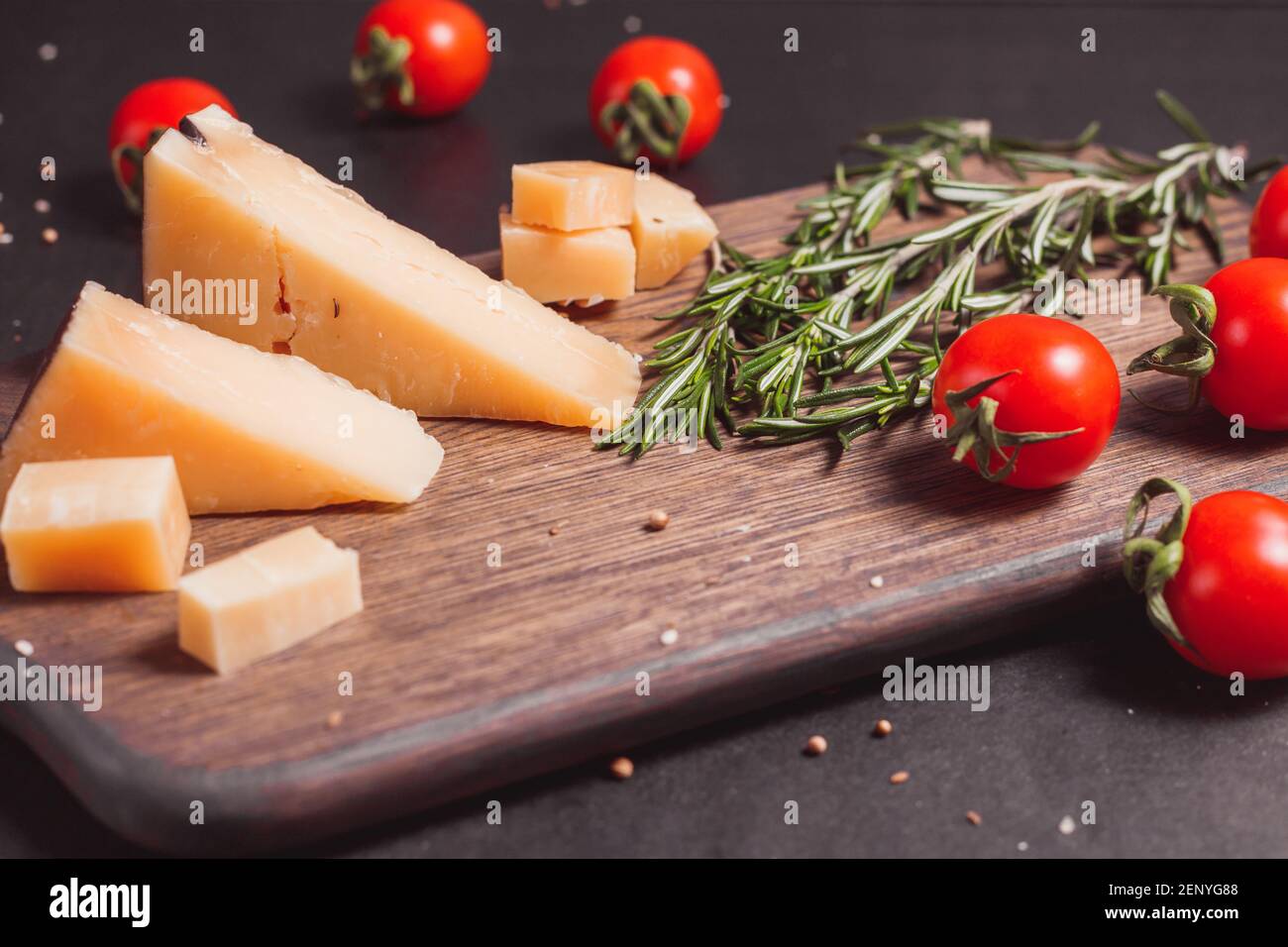Stücke von hartem, gereiftem Käseparmesan, frischen Tomaten und Kräutern auf Holzbrett Stockfoto