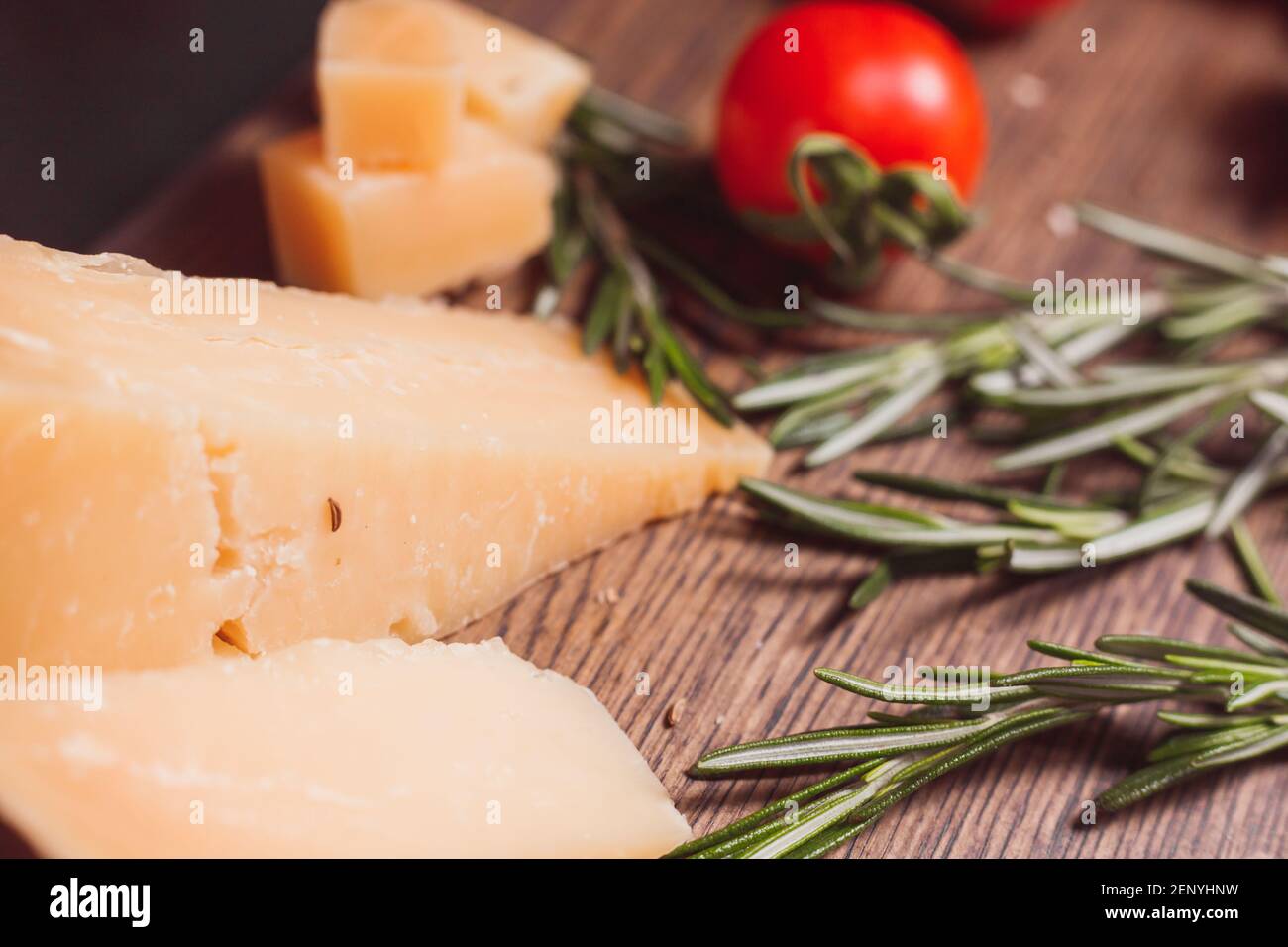 Stücke von hartem, gereiftem Käseparmesan, frischen Tomaten und Kräutern auf Holzbrett Stockfoto