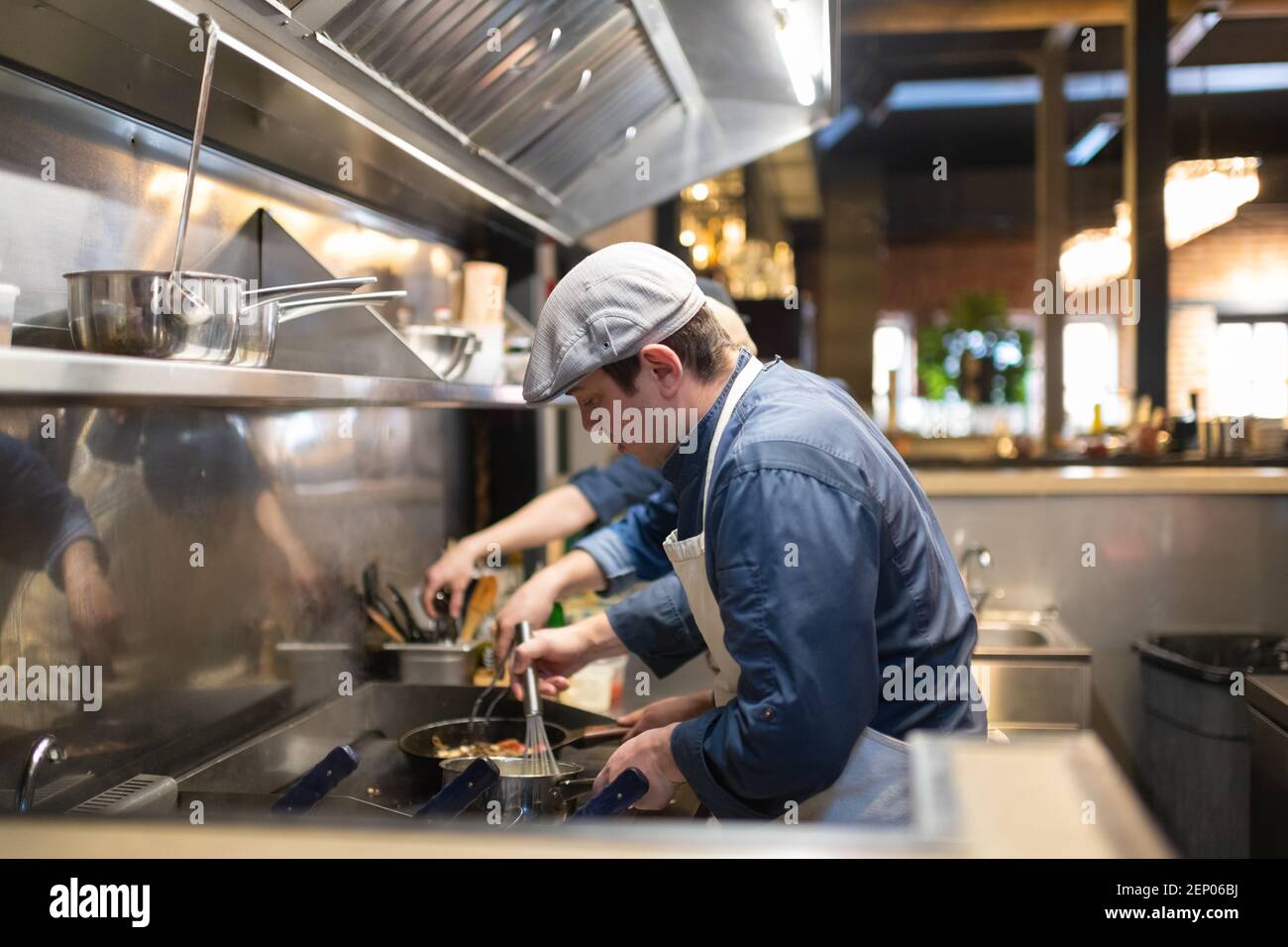 Männlicher Koch in Kappe Rühren Sauce in Topf auf Herd Während der Arbeit in Café-Küche Stockfoto