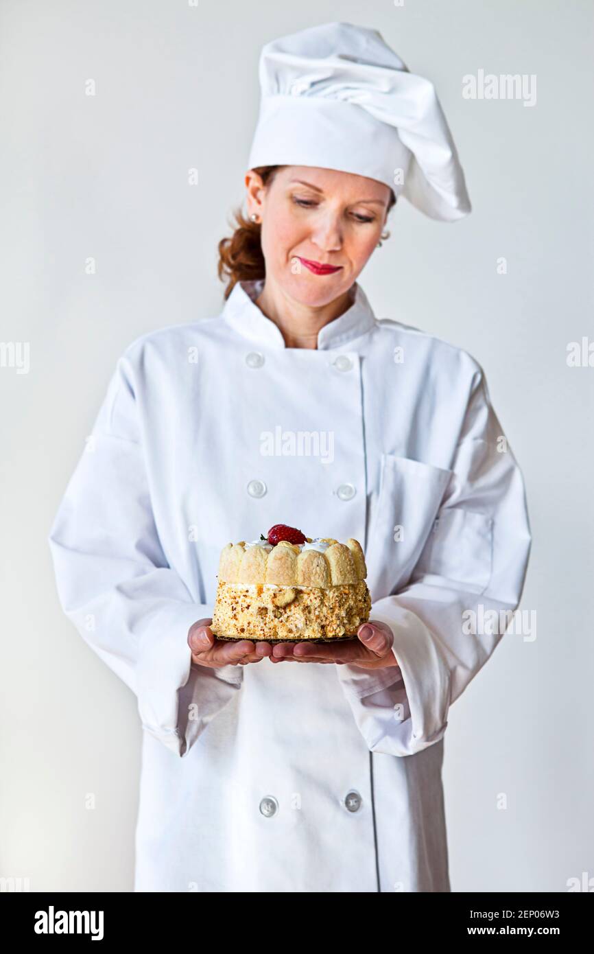 Eine Köchin hält einen Kuchen in einem traditionellen weißen Chefmantel und Hut. Geringe Schärfentiefe mit Fokus auf den Kuchen. Stockfoto