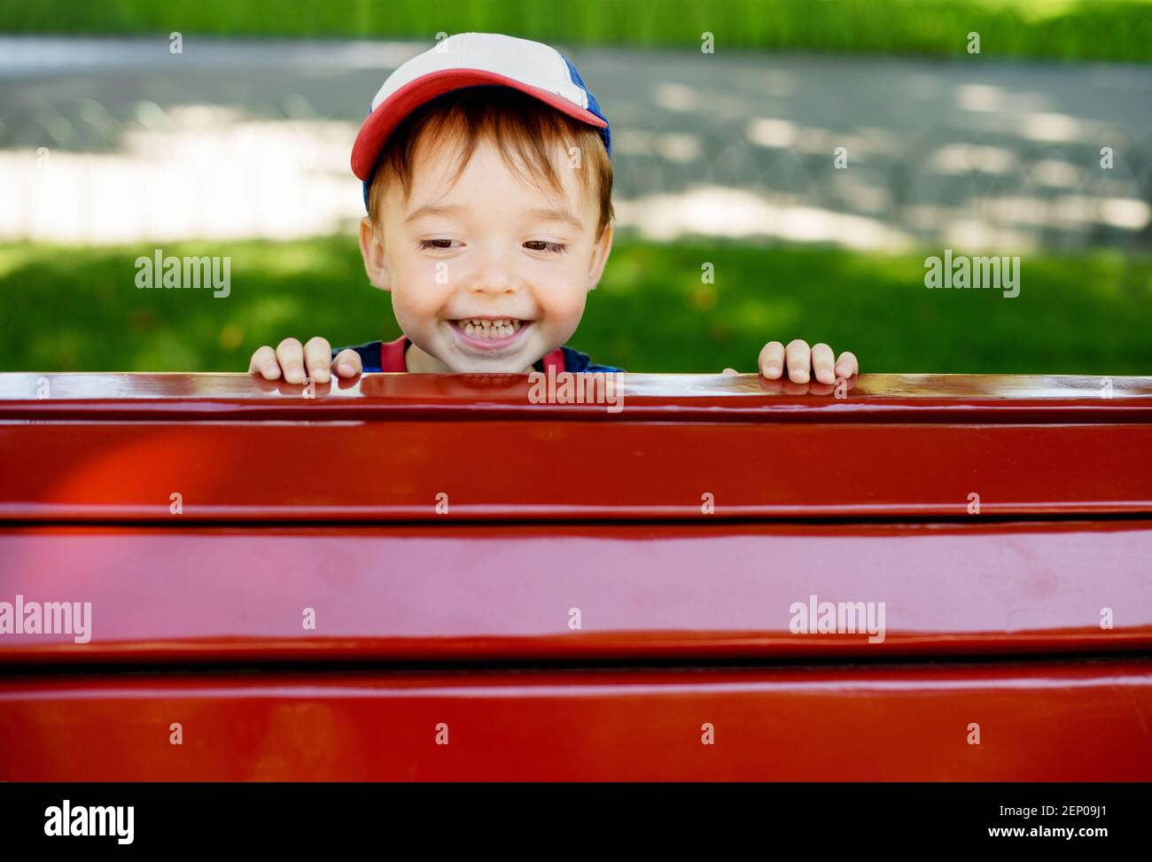Nettes Kleinkind lächelnd glücklich spähen aus hinter Red Park Bank Stockfoto