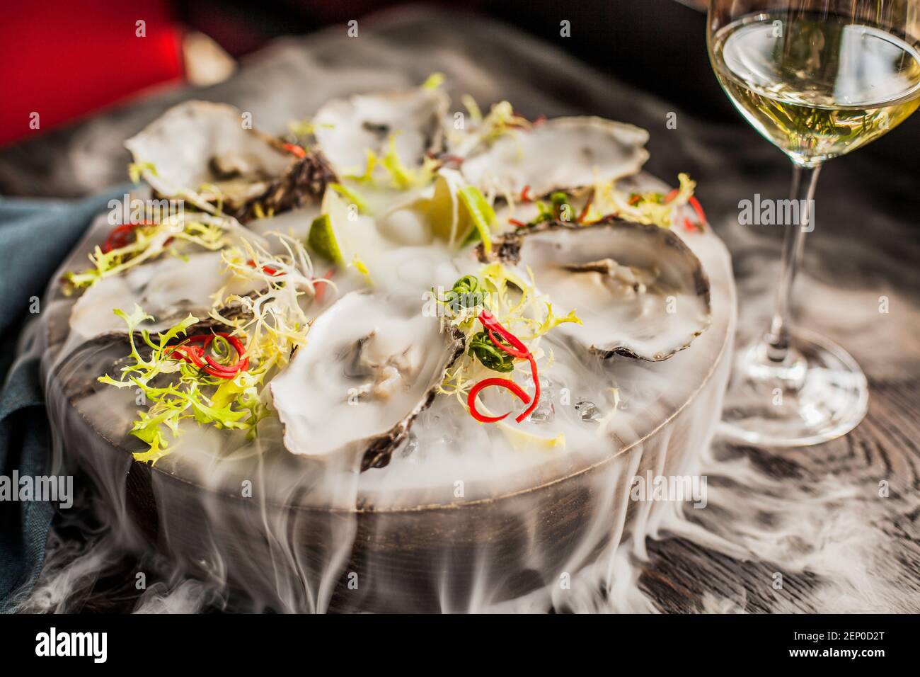 Eine Platte mit Austern in Rauch und ein Glas Weißwein in der Nähe Stockfoto