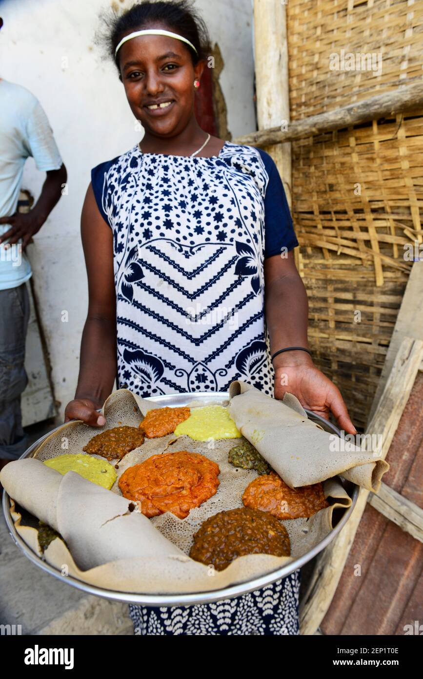 Eine äthiopische Kellnerin präsentiert ein traditionelles Injera-Gericht mit verschiedenen Gemüsesorten und Saucen. Stockfoto