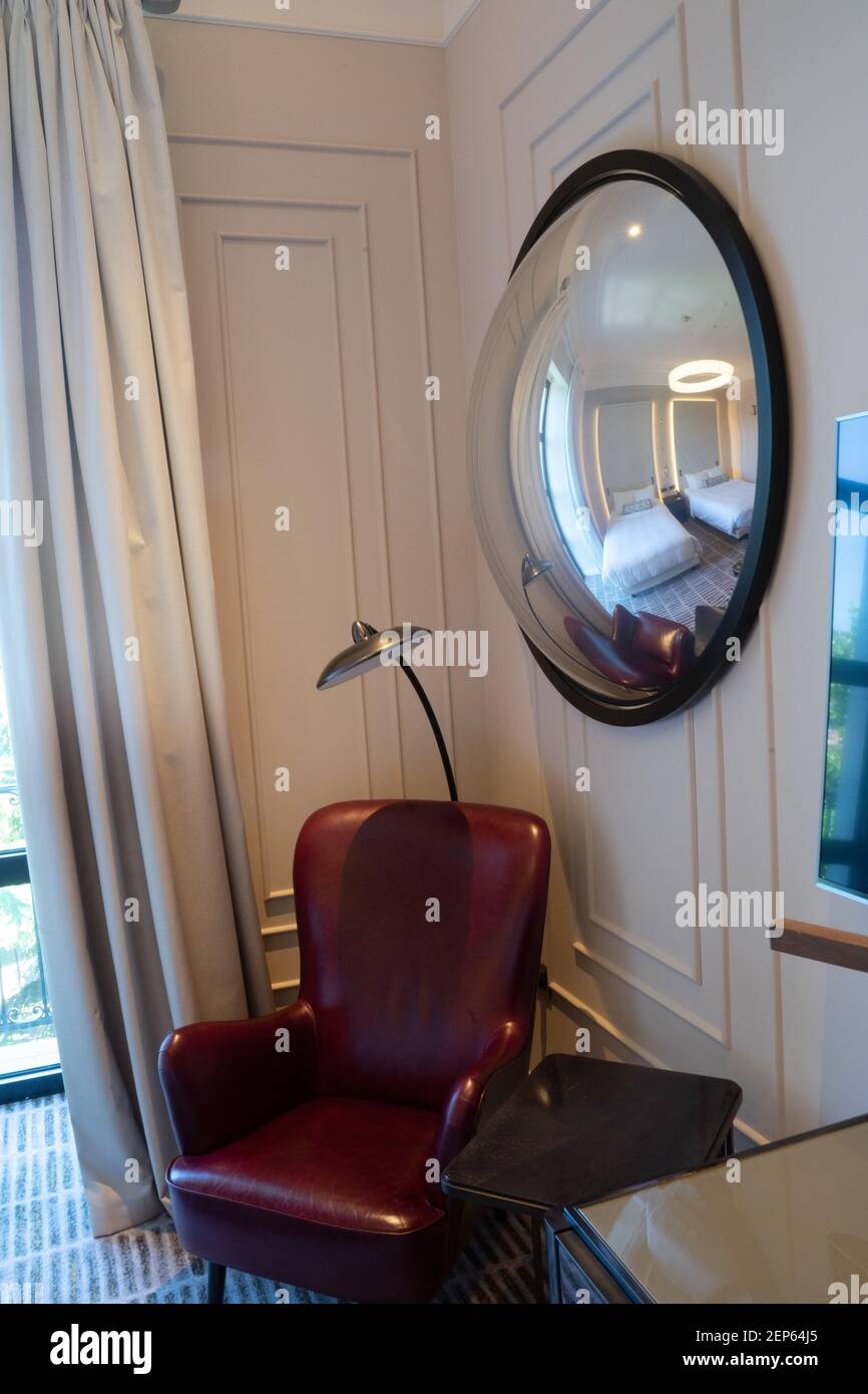 Ein großer kugelförmiger Spiegel, der die Einzelbetten des modernen Luxuszimmers reflektiert, unter Tageslicht mit einem luxuriösen, komfortablen Stuhl Stockfoto