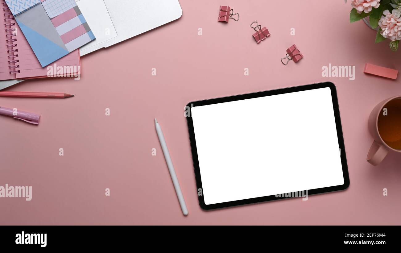 Draufsicht auf den stilvollen Arbeitsplatz mit digitalem Tablet, Eingabestift, Notebook und Kaffeetasse auf pinkem Tisch. Stockfoto