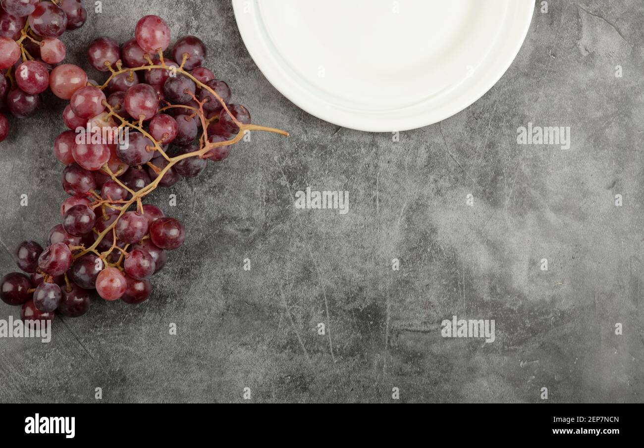 Weißer Teller und rote köstliche Trauben auf Marmortisch Stockfoto