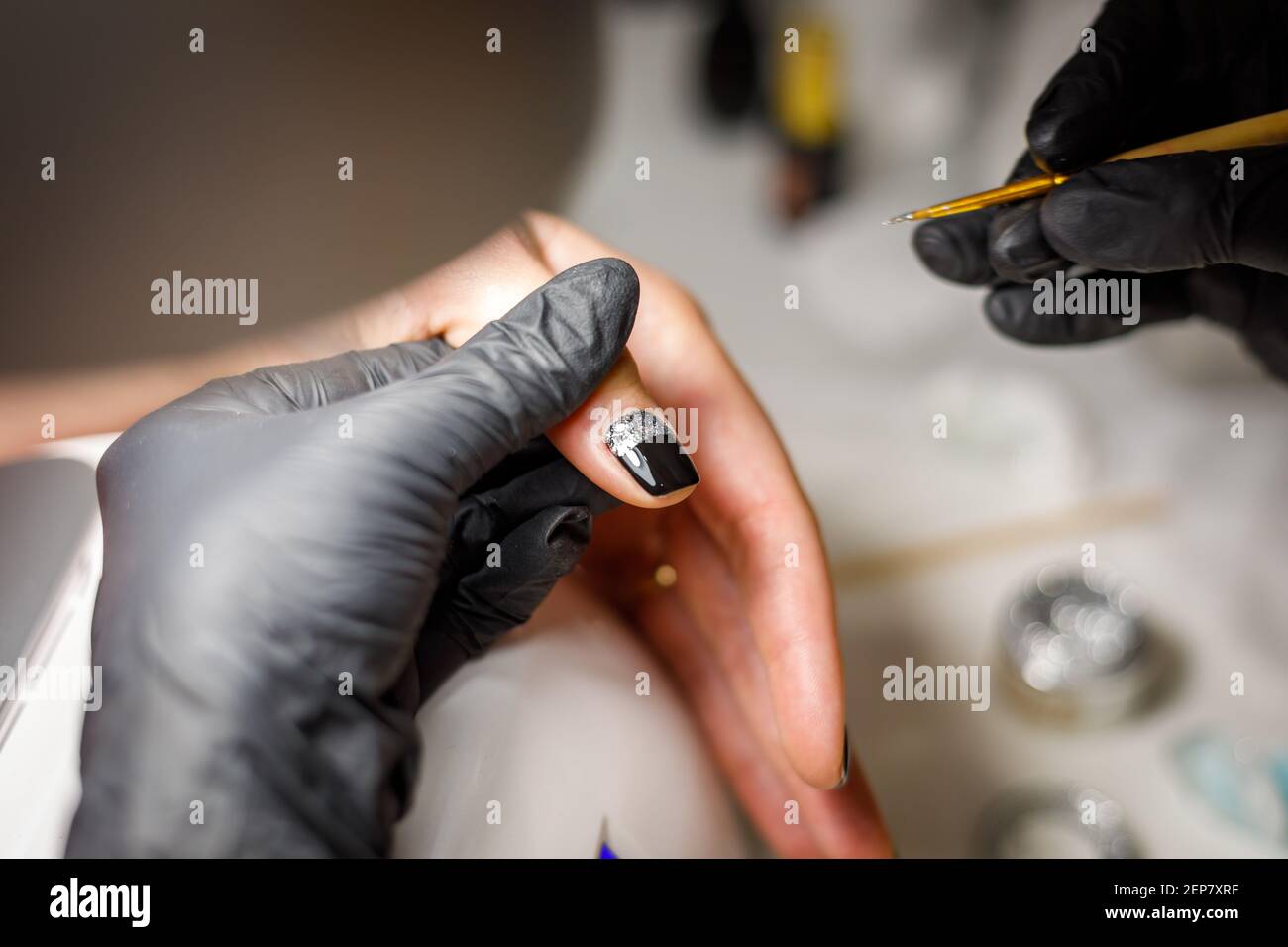 In einem Schönheitssalon macht der Meister eine Maniküre, trägt ein Muster auf den Nagel mit einem Pinsel, schwarzer Lack mit einem goldenen Muster. Stockfoto