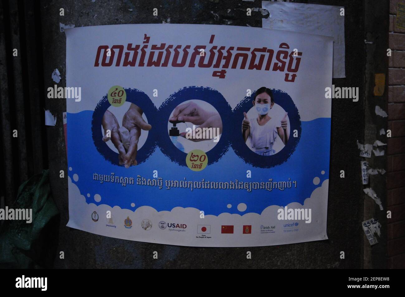 Während eines Ausbruchs von COVID - 19, USAID stellt Plakate in Khmer-Skript warnen Menschen, ihre Hände zu waschen, verwenden Händedesinfektionsmittel & tragen Gesichtsmasken, in einem Slum in der Nähe von Kandal Markt, während der Coronavirus-Pandemie. Phnom Penh, Kambodscha. © Kraig Lieb Stockfoto