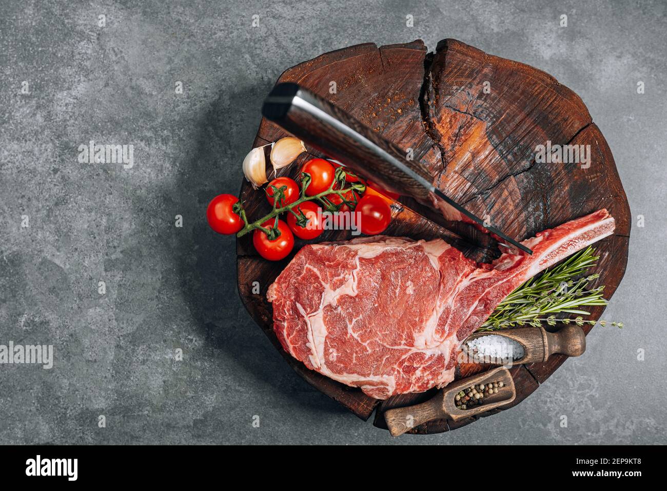 Auf einem Holzblock für Fleisch ein frisches rohes tamahawk Steak oder ein Cowboy Steak mit einer Metzgerhackaxt für Fleisch, daneben eine Mischung aus Paprika und Stockfoto