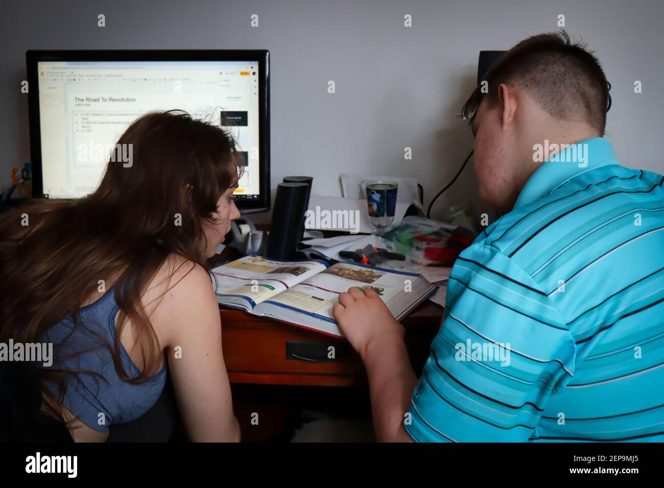 Teenager Junge hilft seiner Schwester mit Hausaufgaben auf einem unordentlichen Schreibtisch in einem Heimbüro. Stockfoto