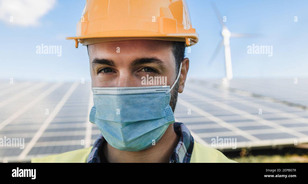 Junger Mann, der im Solarkraftwerk arbeitet und dabei Sicherheit trägt Gesichtsmaske für Coroanvirus Ausbruch - Eco-Konzept - weich Fokus auf Augen Stockfoto