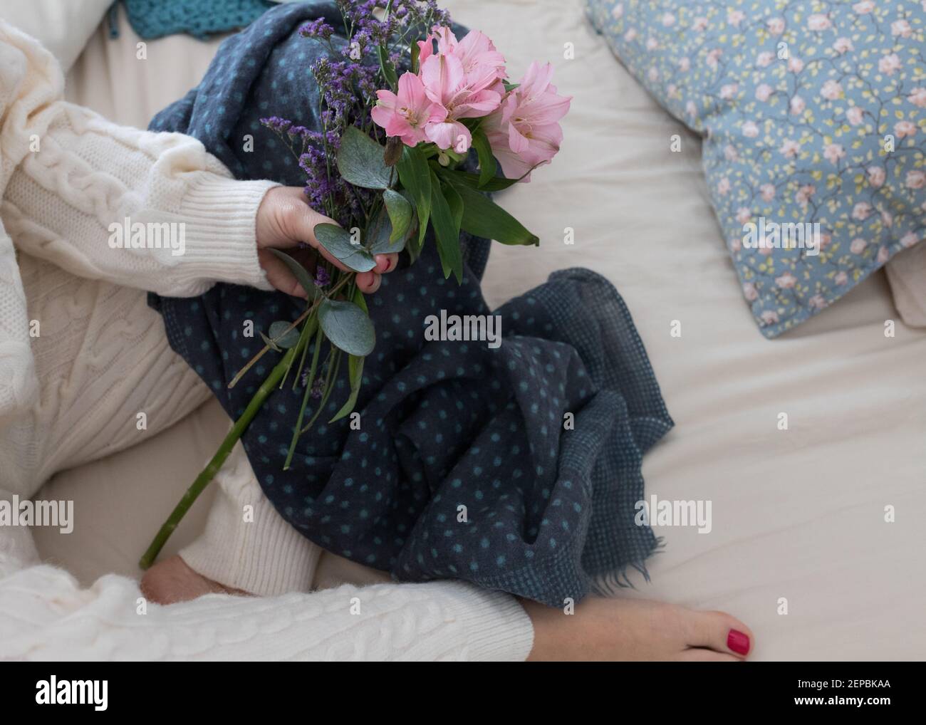 Bouquet von rosa und lila Blumen von einer Frau auf Wolle Loungewear gekleidet gehalten. Stockfoto