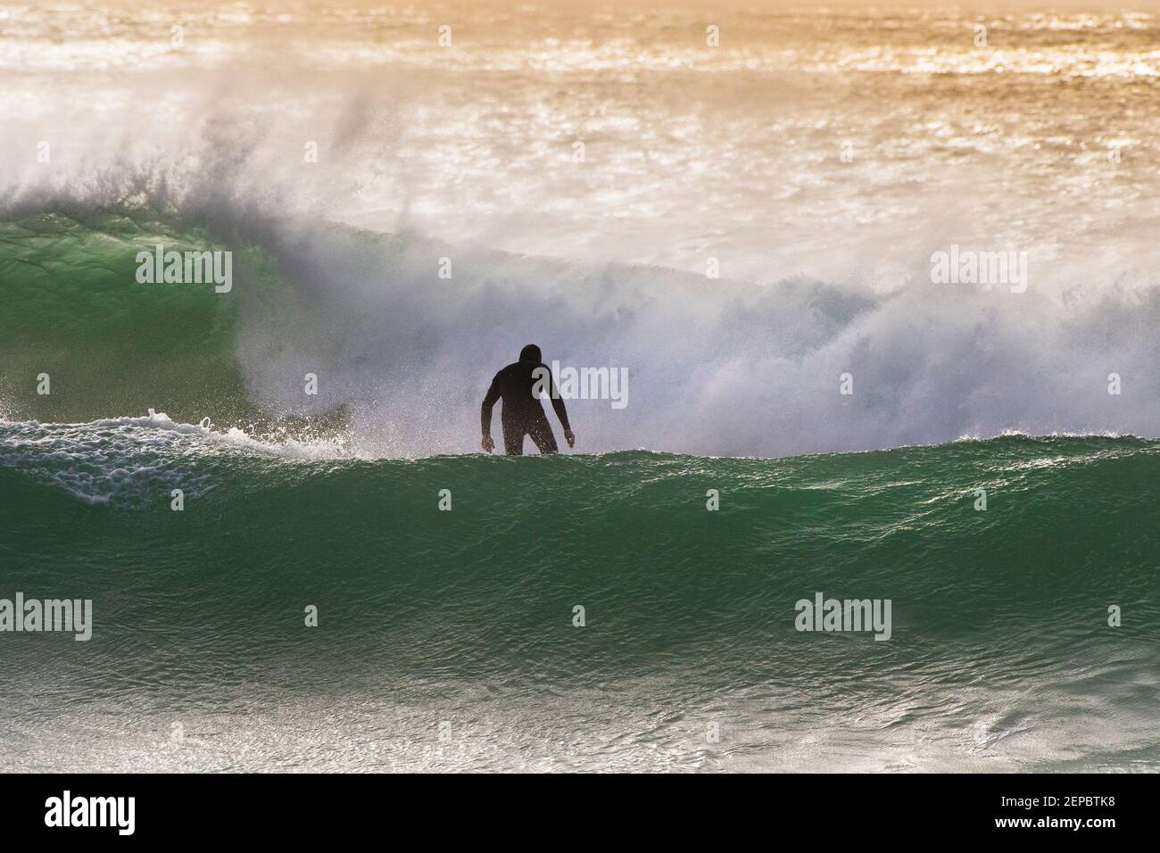 Die Figur eines Surfers zwischen riesigen Wellen am Fistral in Newquay in Cornwall. Stockfoto