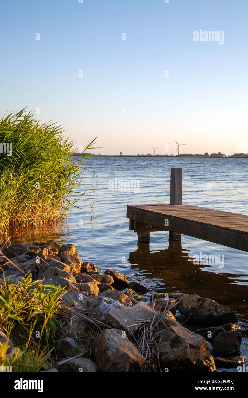 Schöne ruhige Wasserlandschaft in warmen Sonnenuntergang Licht in Friesland, Niederlande. Felsen und Schilf auf der linken Seite, und ein Gerüst auf der rechten Seite Stockfoto