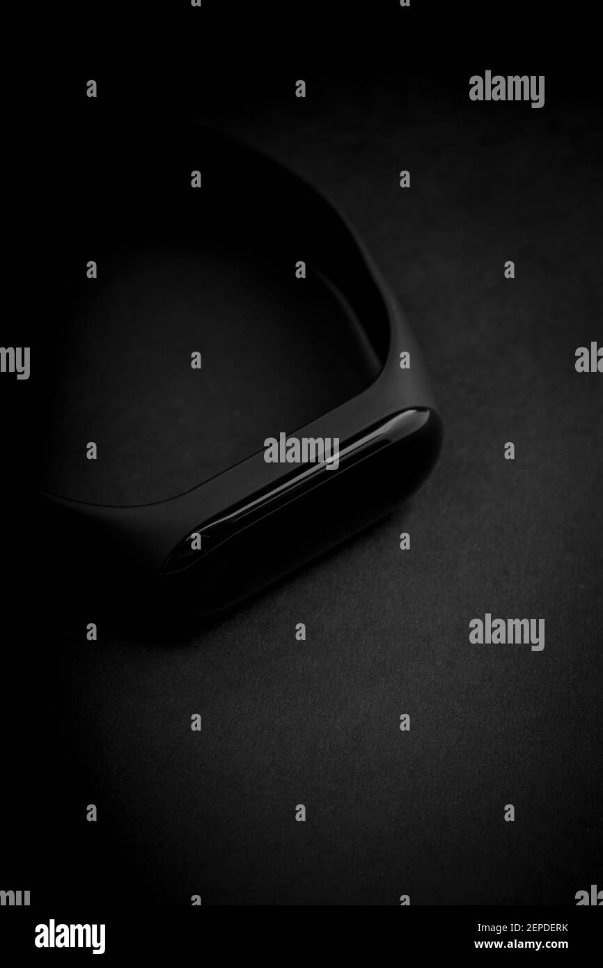 Schwarze elektronische Uhr und Smart Fitness Tracker auf texturiertem schwarzem Hintergrund. Dunkles Objekt auf dunklem Hintergrund. Dunkle Luxus-Stimmung. Modisches Accessoire Stockfoto