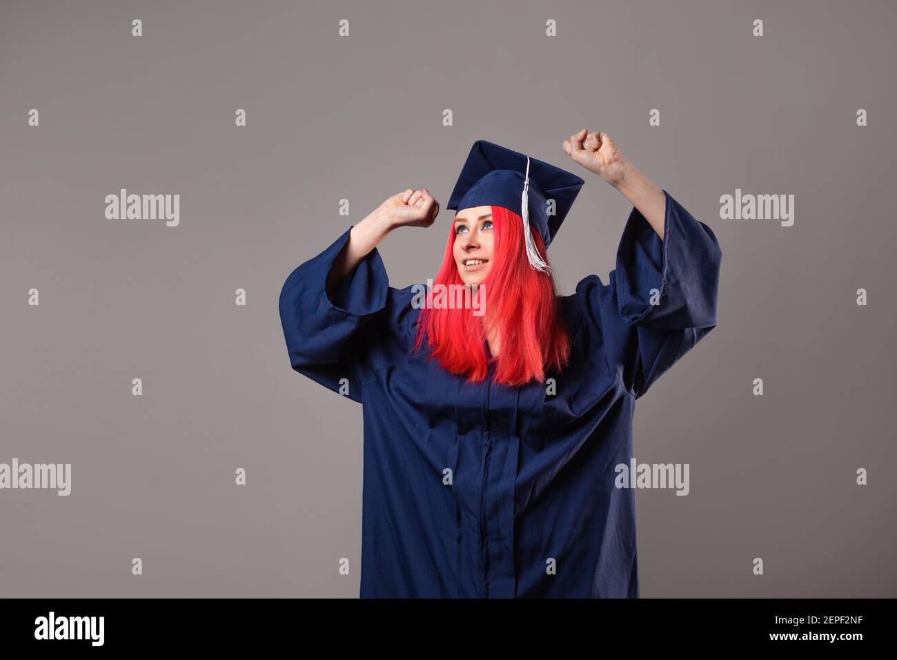 Glücklicher Absolvent auf grauem Hintergrund. Eine junge Frau mit hellen Haaren mit einer Abschlusskappe und einer Robe. Kreative Berufe, Kunst und Wissenschaften. Stockfoto