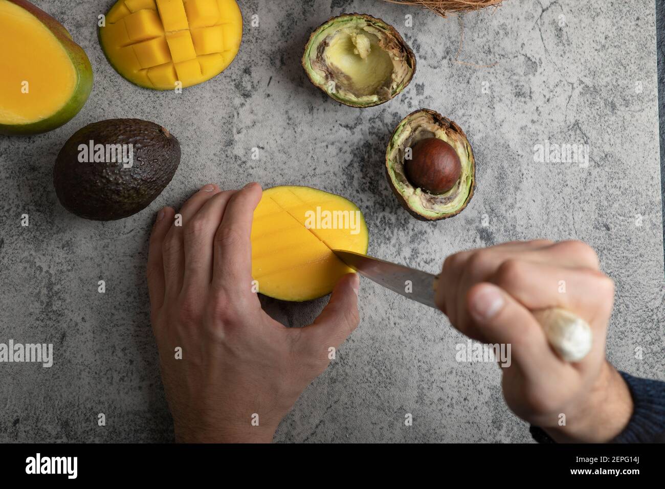 Männliche Hände schneiden Mango in die Würfel auf Marmoroberfläche Stockfoto