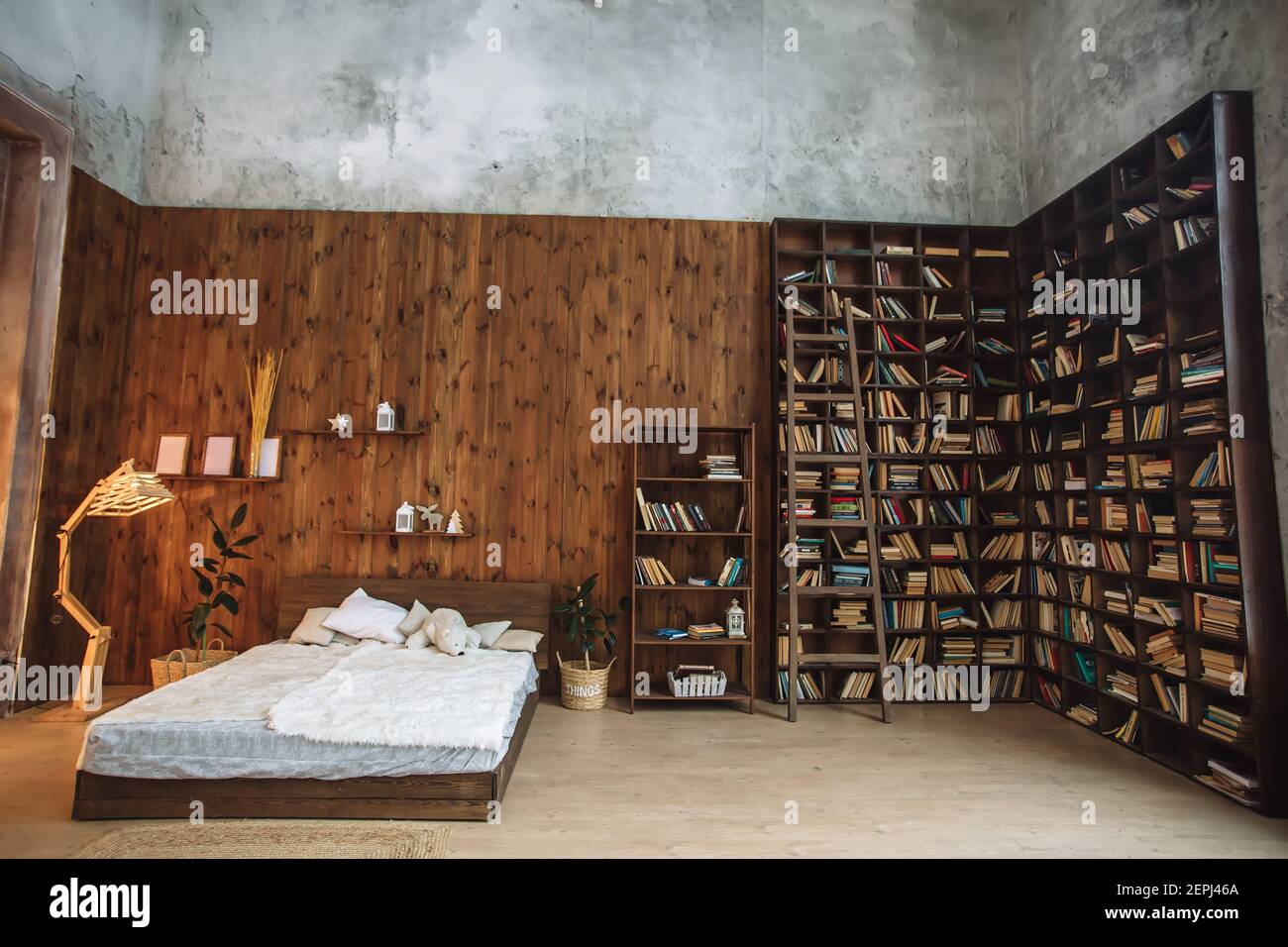 Helles Interieur des Schlafzimmers mit Holzwand, ein Holzbett mit weißem, Loft-Interieur mit dekorativer Lampe und Bücherregale im Studio Stockfoto