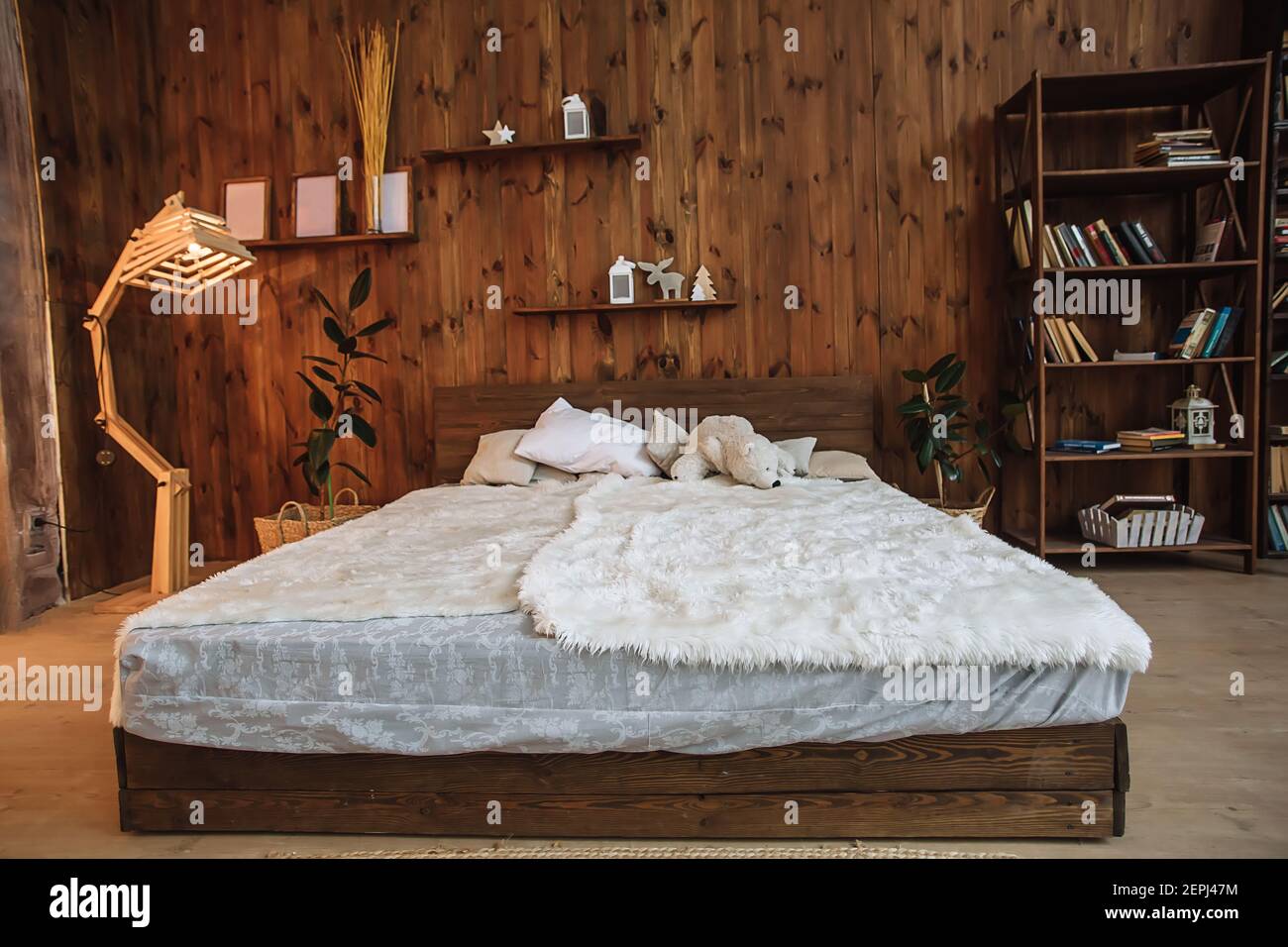 Helles Interieur des Schlafzimmers mit Holzwand, ein Holzbett mit weißem, Loft-Interieur mit dekorativer Lampe und Bücherregale im Studio Stockfoto
