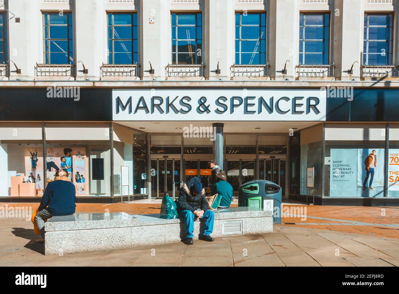 Die Leute sitzen auf einer Marmorbank vor dem Marks & Spencer Store in der Broad Street in Reading, Großbritannien. Der Shop wird wegen einer durch COVID verursachten Sperrung geschlossen. Stockfoto