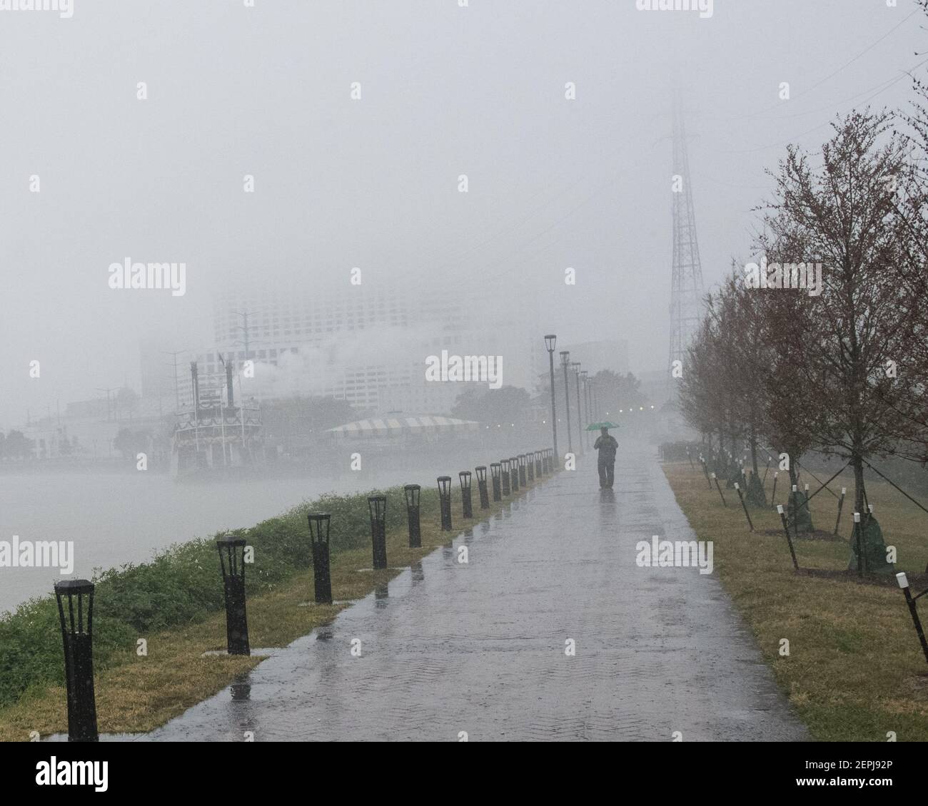 Silhouettenfiguren mit Regenschirmen spazieren entlang des nebelverhangenen Mississippi-Flussufers, vorbei am historischen Dampfschiff Natchez in New Orleans. Stockfoto