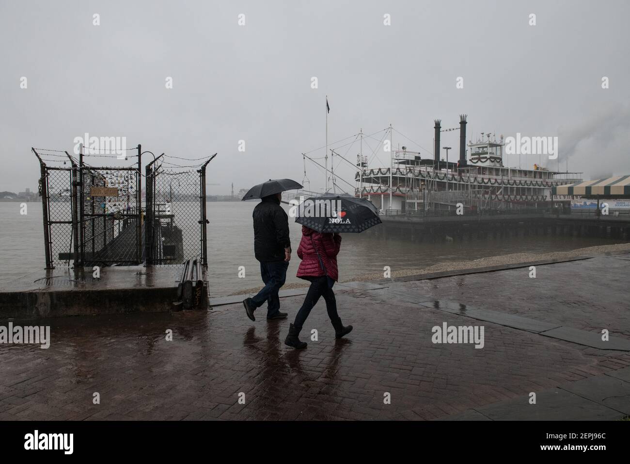 Silhouettenfiguren mit Regenschirmen spazieren entlang des nebelverhangenen Mississippi-Flussufers, vorbei am historischen Dampfschiff Natchez in New Orleans. Stockfoto
