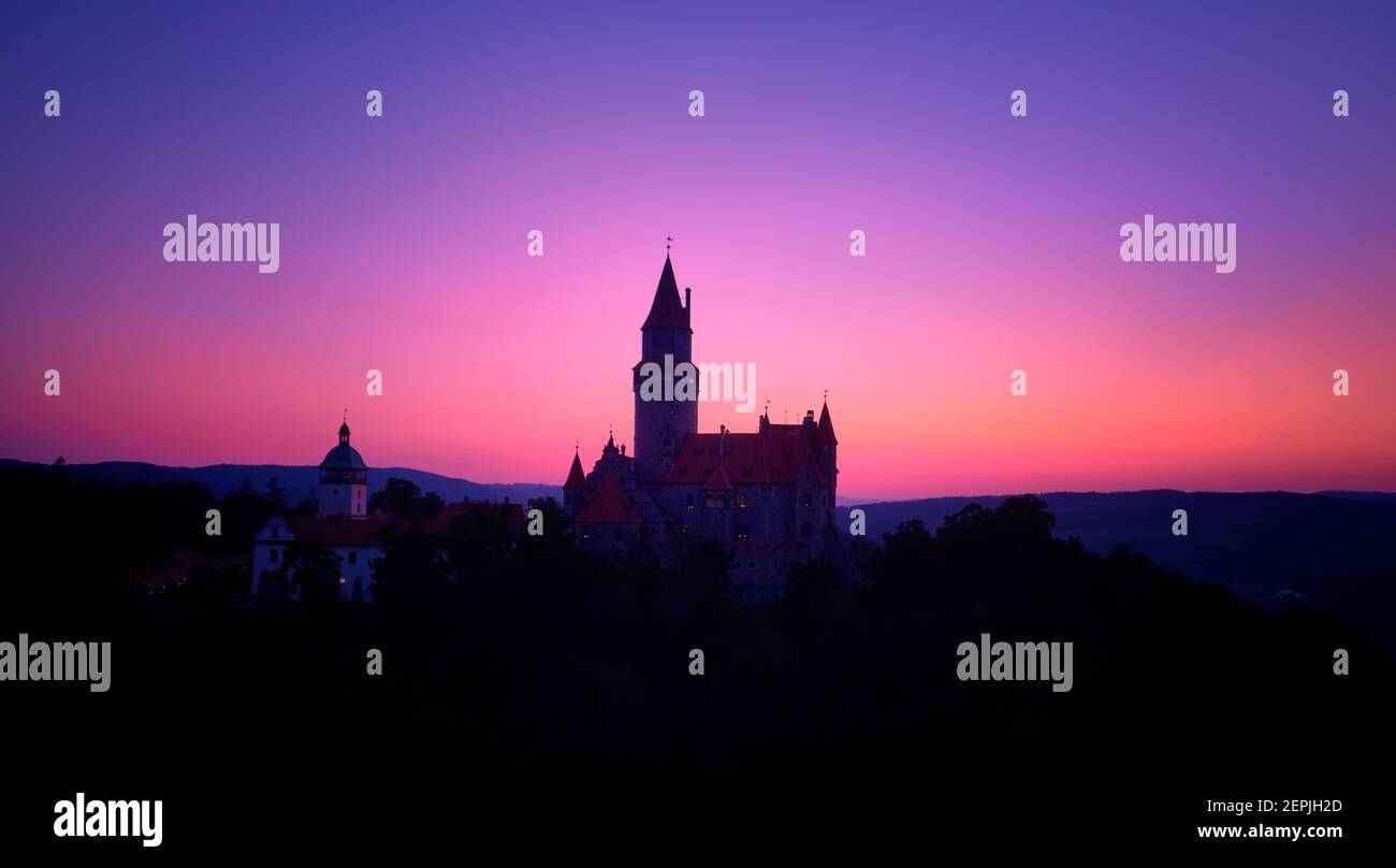 Luftaufnahme einer Silhouette eines romantischen Märchenschlosses gegen den rosa und violetten Abendhimmel. Schloss Bouzov mit vielen Türmen, touristischer Ort auf Mähren. Stockfoto