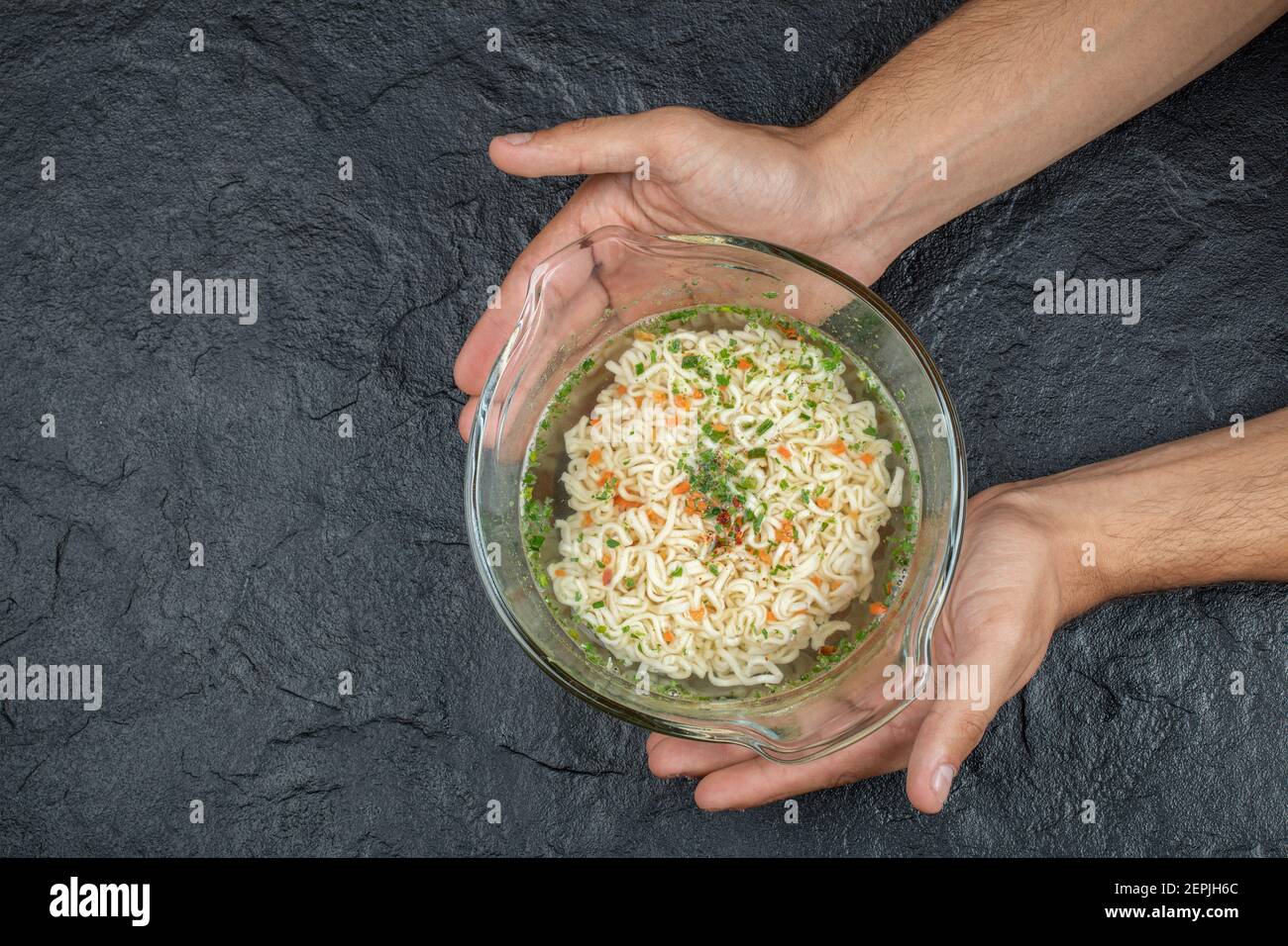 Hand hält eine Glasplatte mit leckeren Nudeln auf einem Dunkler Hintergrund Stockfoto