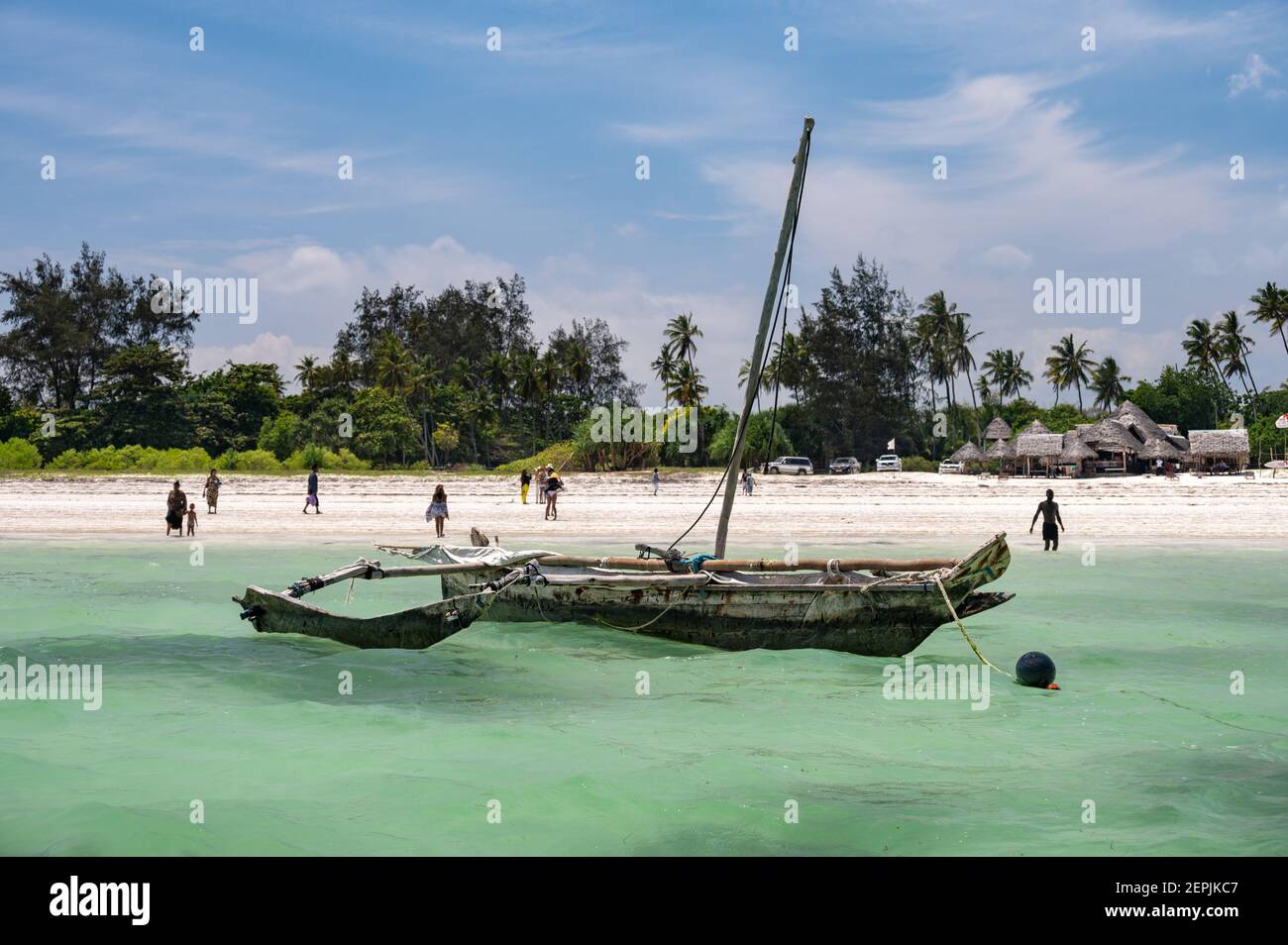 Ein traditionelles Fischerboot aus Mangobaum am Ufer mit Menschen am Strand dahinter, Diani, Kenia, Ostafrika Stockfoto