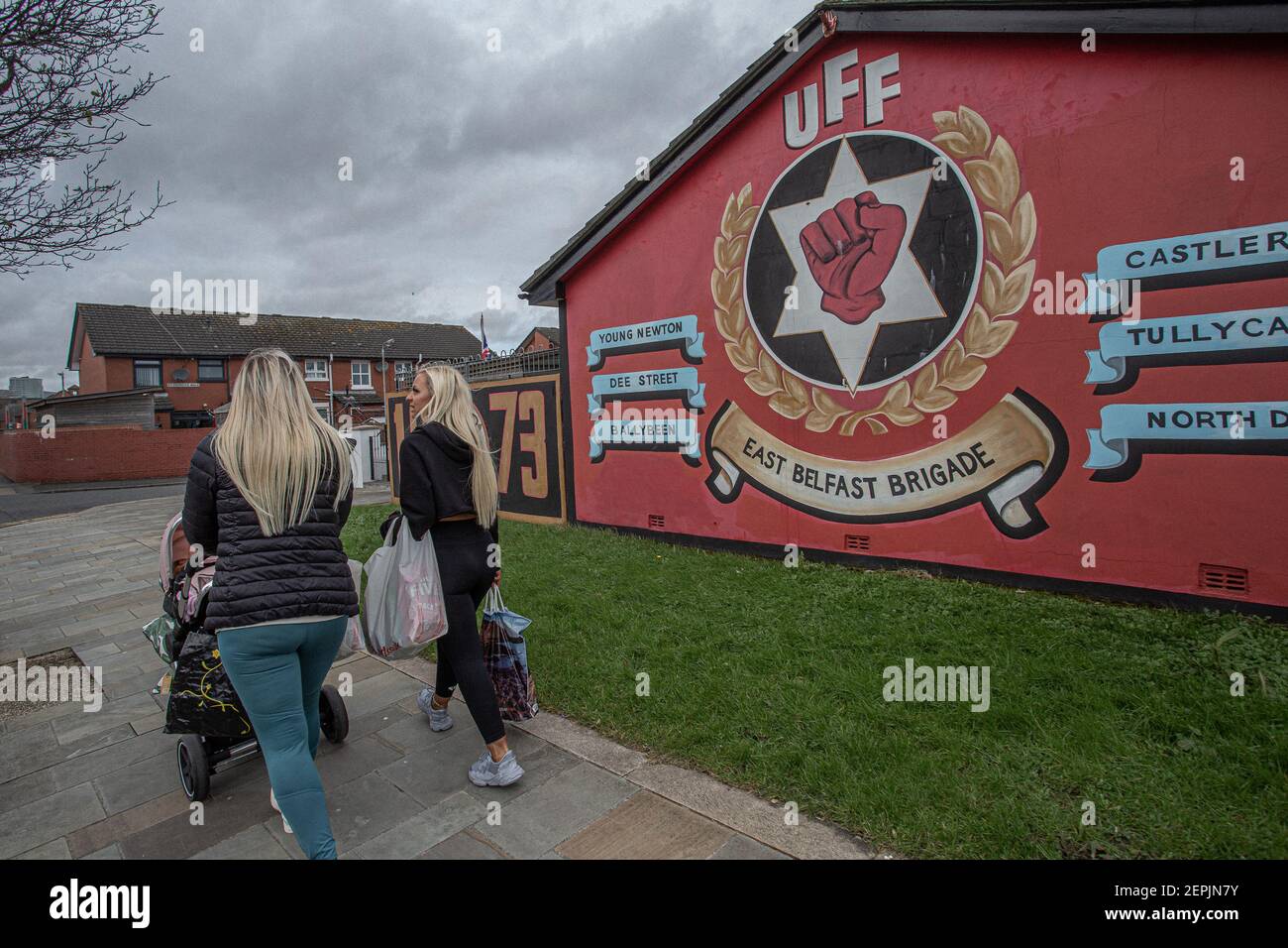 BELFAST, NORDIRLAND - Februar 24: Zwei Frauen gehen an Loyalisten-Wandgemälden in 'Freedom Corner', Newtownards Road, Belfast vorbei.hauptsächlich Pro der Arbeiterklasse Stockfoto
