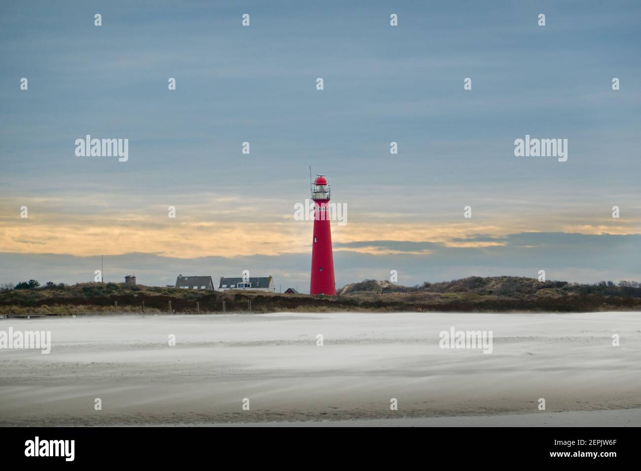 Blick auf den roten Leuchtturm der niederländischen Insel Schiermonnikoog über einen Strand, Sturm weht Sand über den Strand Stockfoto