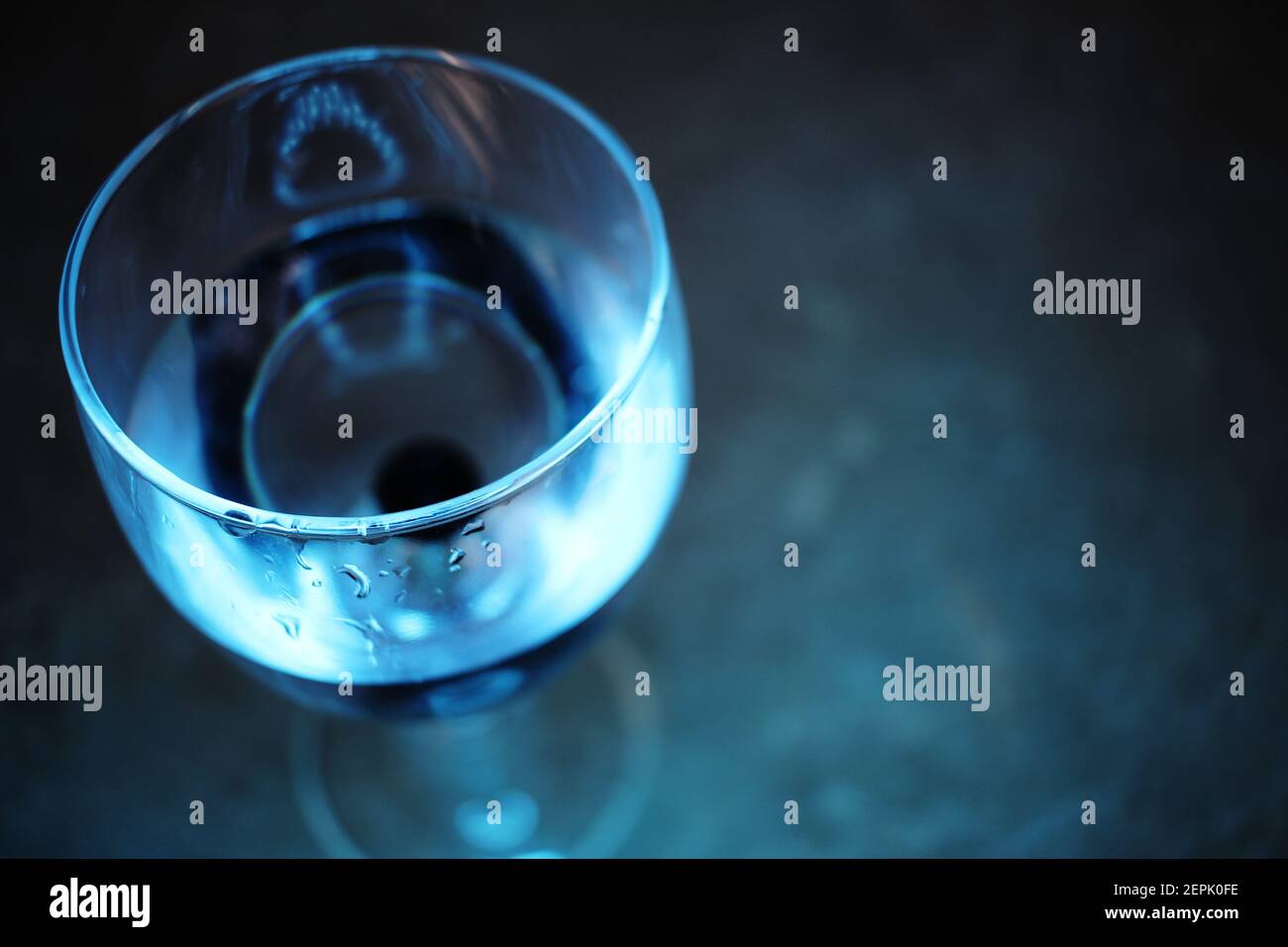 Weinglas unter blauem Licht halb mit Wasser gefüllt. Stockfoto