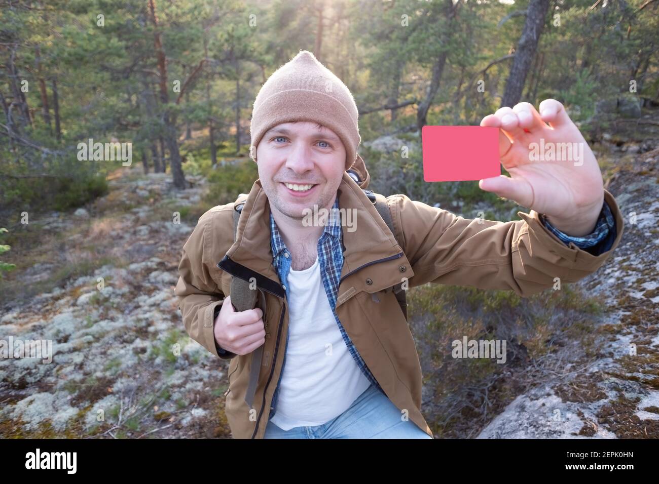 Junger lächelnder Mann zeigt leere Kreditkarte beim Wandern. Konzept des einfachen Reisens Stockfoto
