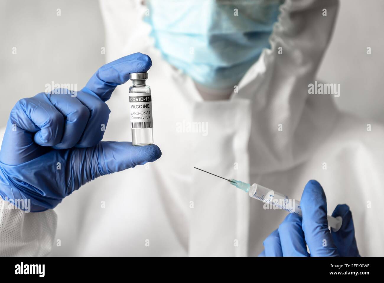 COVID-19-Impfstoff in Arzthand, Krankenschwester in weißem medizinischen PSA-Anzug hält Spritze und Coronavirus-Impfstoffflasche. Arzt in Maske und Medikament für Schuss. C Stockfoto