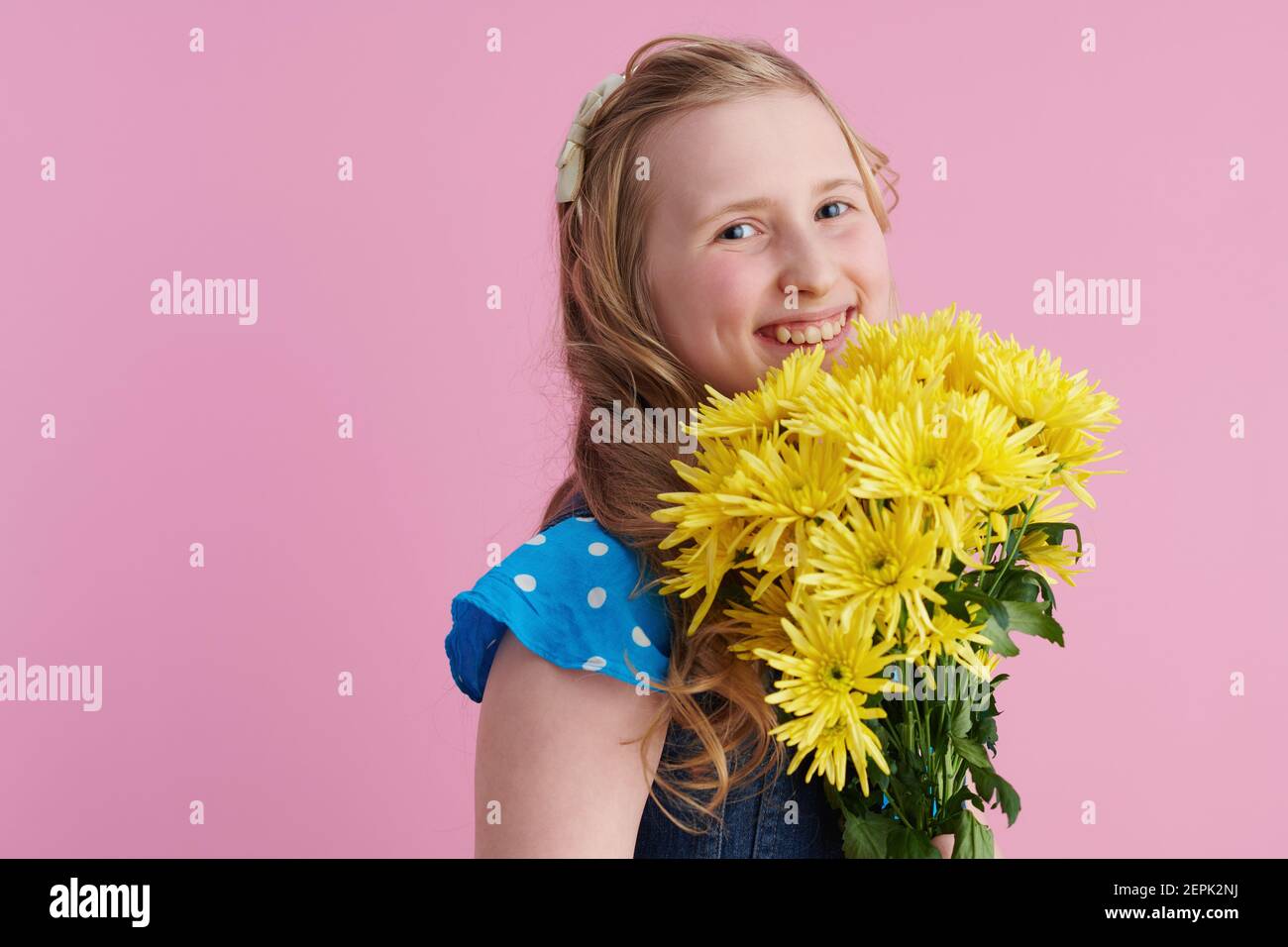 Portrait von glücklichen modernen Mädchen mit langen welligen blonden Haaren mit gelben Chrysanthemen Blumen vor rosa Hintergrund. Stockfoto
