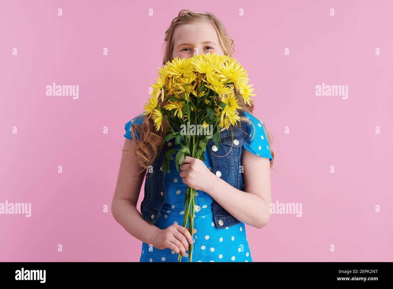 Happy modernes Mädchen mit langen welligen blonden Haaren mit gelben Chrysanthemen Blumen isoliert auf rosa. Stockfoto