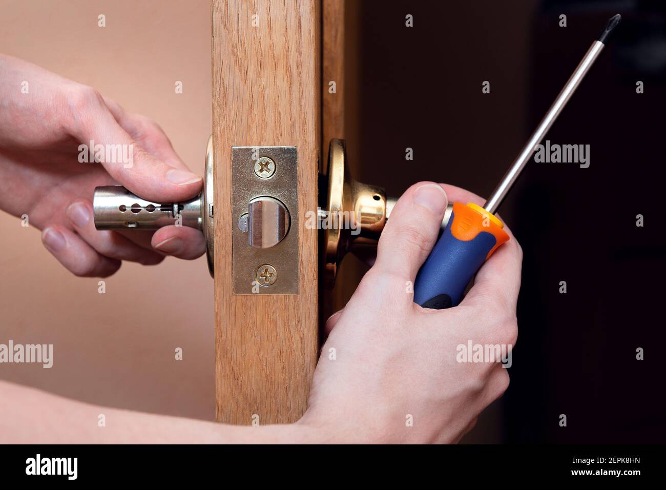 Türinstallation, Arbeiter installiert Türknauf, Holzarbeiter Hände aus der Nähe. Ein Mann dreht den Türgriff mit einem Schraubendreher, repariert den Türgriff mecha Stockfoto