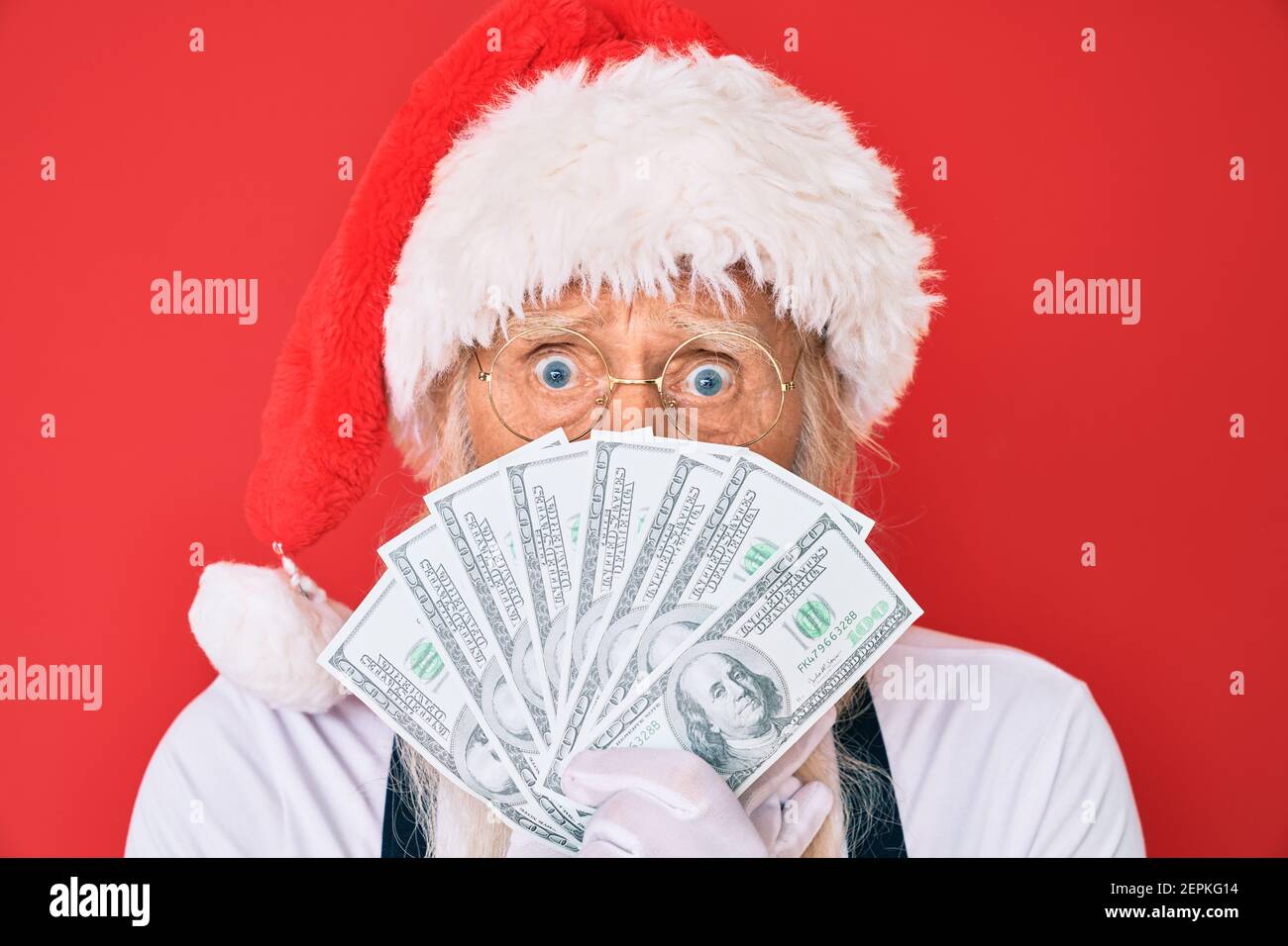 Alter älterer Mann mit grauen Haaren und langem Bart trägt weihnachtsmann Kostüm hält Dollar decken Mund mit der Hand, schockiert und Angst vor Fehler. Sur Stockfoto