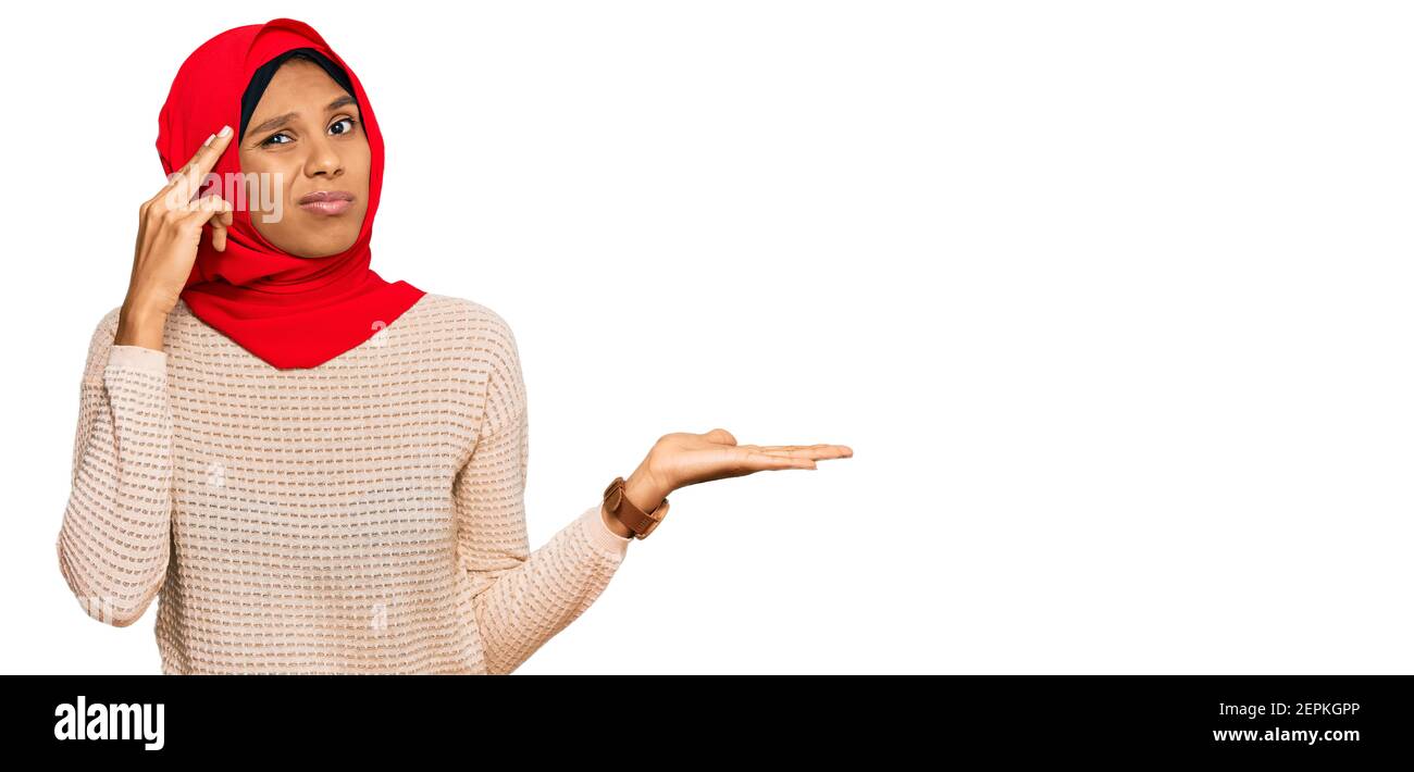 Junge afroamerikanische Frau trägt traditionelle islamische Hijab Schal verwirrt Und ärgerlich mit offener Handfläche, die Kopieplatz und Zeigepointing zeigt Finger auf für Stockfoto