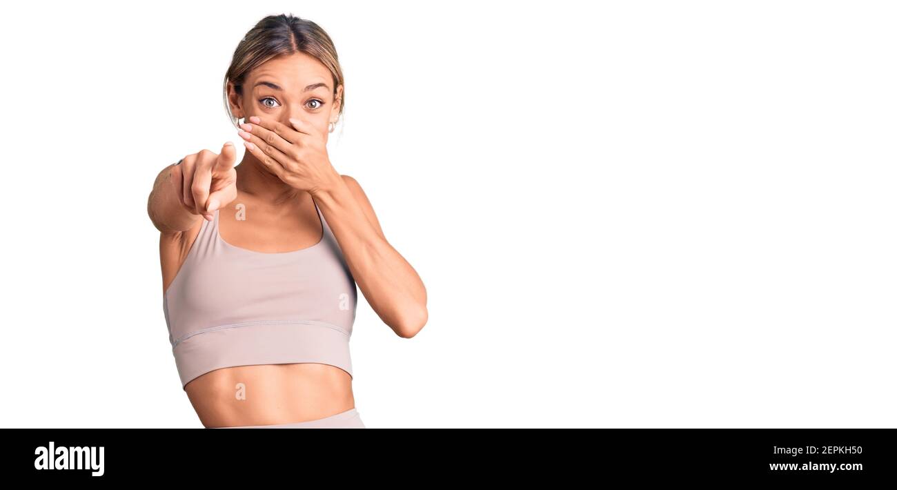 Schöne kaukasische Frau trägt Sportkleidung lachend auf Sie, zeigt Finger auf die Kamera mit Hand über Mund, Scham Ausdruck Stockfoto