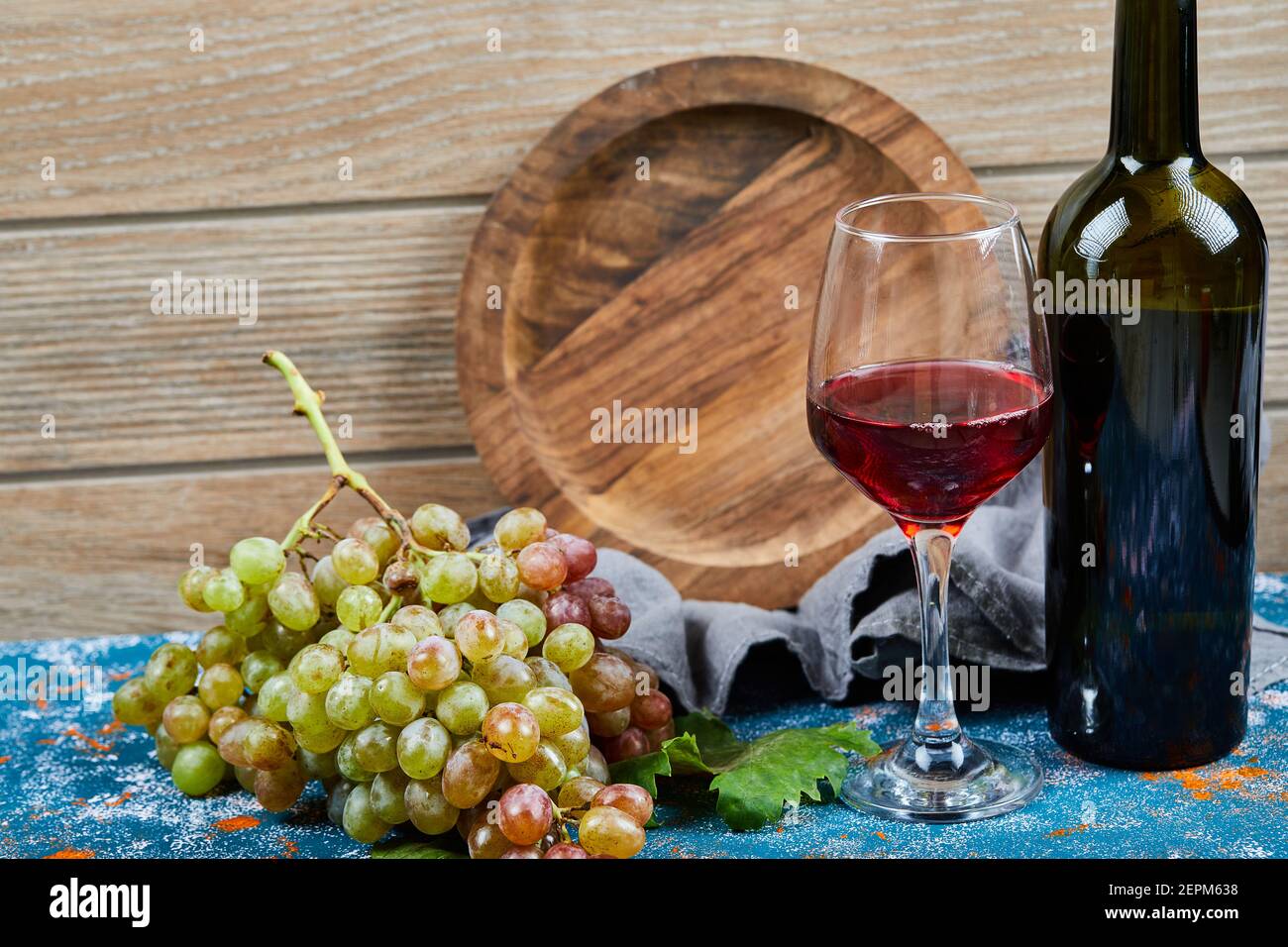 Trauben, ein Glas Rotwein und eine Flasche Wein auf Blau Stockfoto