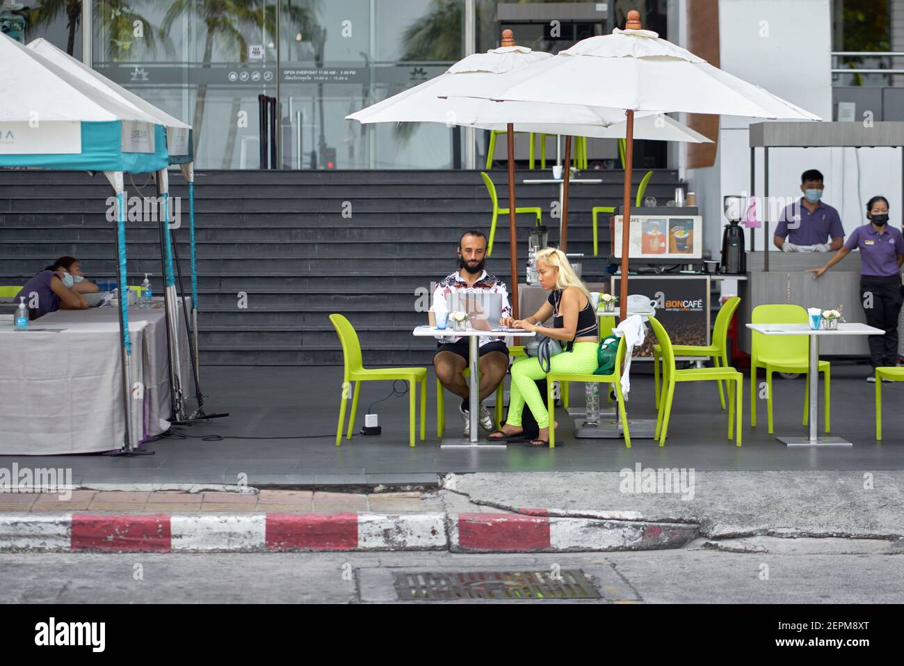 Ein Paar, das Laptops benutzte, saß an einer Kaffeebar auf dem Straßenbelag, während eine Frau bunte grüne Leggings trug. Thailand Südostasien Stockfoto