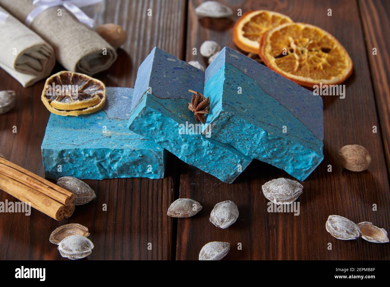 Helle, duftende blaue handgemachte Seife, verschiedene Gewürze und Nüsse auf der dunklen Holzplatte. Stockfoto