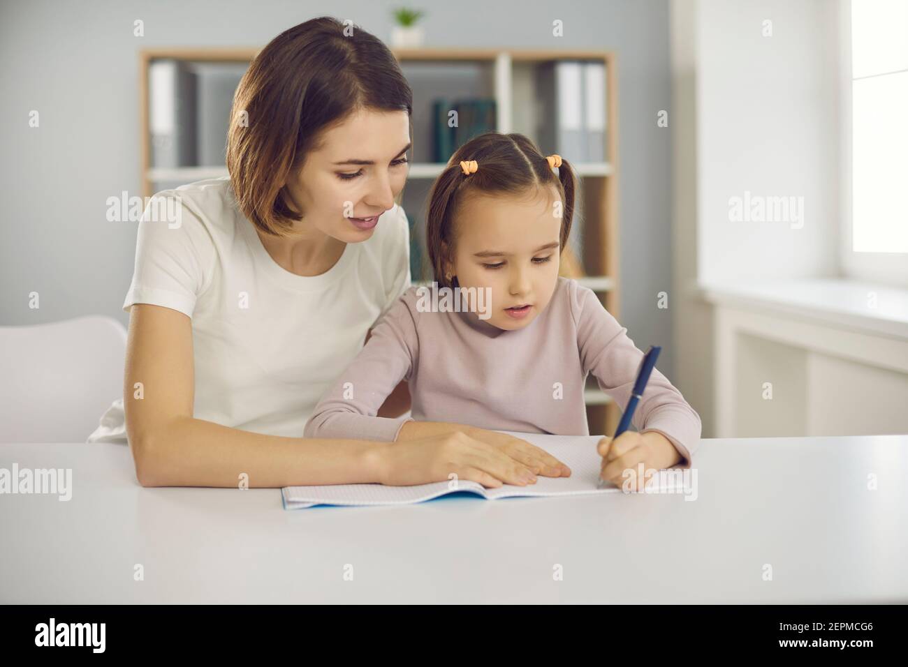 Kleine konzentrierte aufmerksame Mädchen sitzen mit Mutter oder Kindermädchen zusammen Im Zimmer und Zeichnung Stockfoto