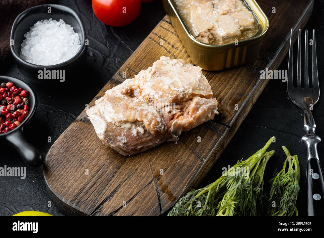 Dosen Wild Alaska Lachs Set, auf Holzschneidebrett, auf schwarzem Hintergrund mit Kräutern und Zutaten Stockfoto